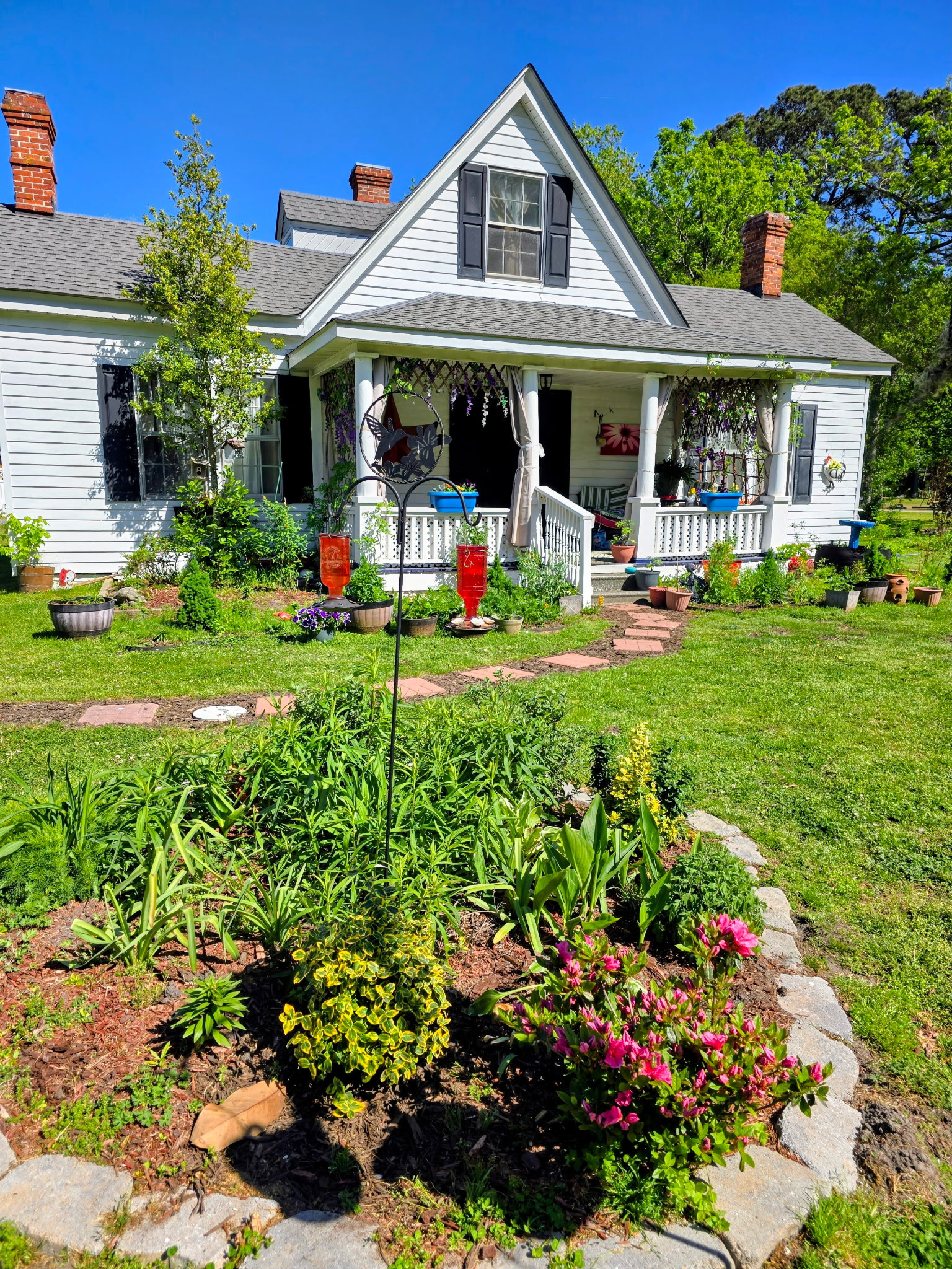 White farmhouse-style home with a front porch, dark shutters, and a large red star on the siding, set on a grassy lawn with trees framing the view belonging to Sponsored Residential Provider Angela Justice in Mathews, Virginia.