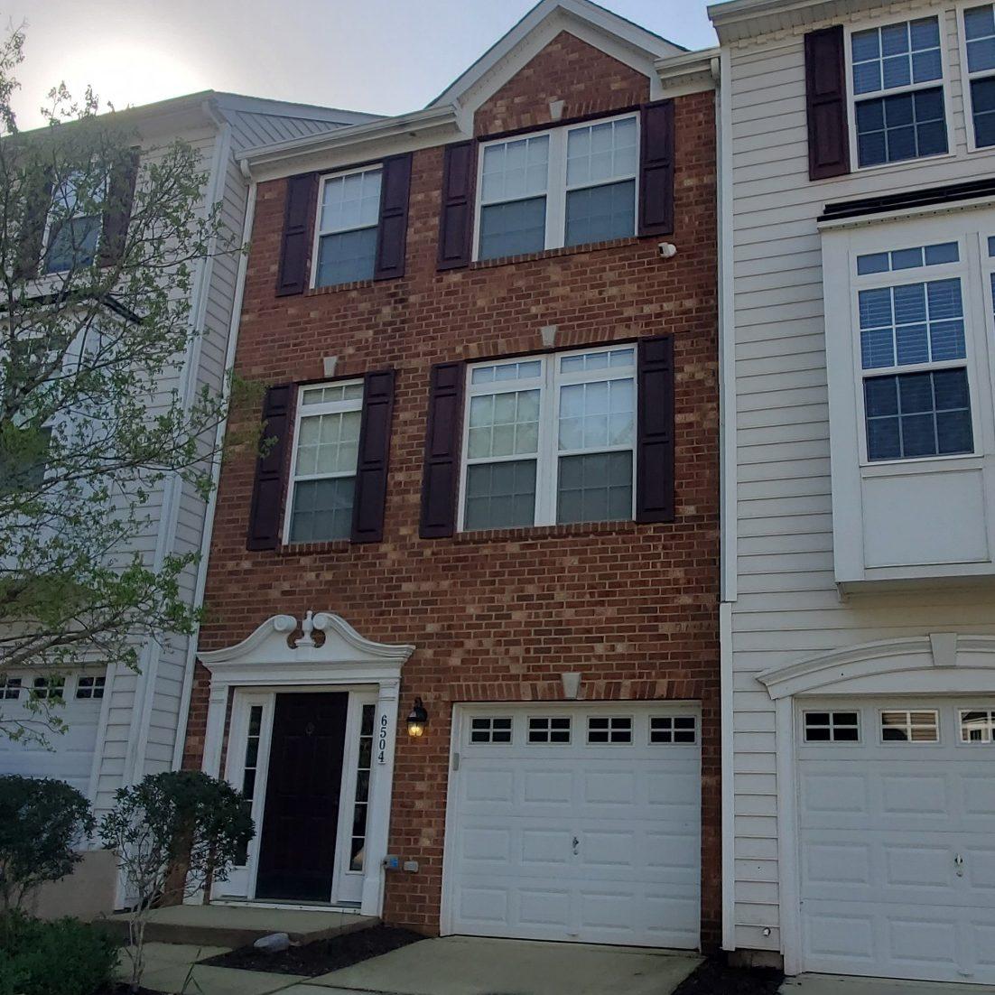 Three‑story townhomes with brick and light siding, front‑facing garages, and a tree‑lined cul‑de‑sac in a residential community belonging to Sponsored Residential Provider Jose Soto in Williamsburg, VA,