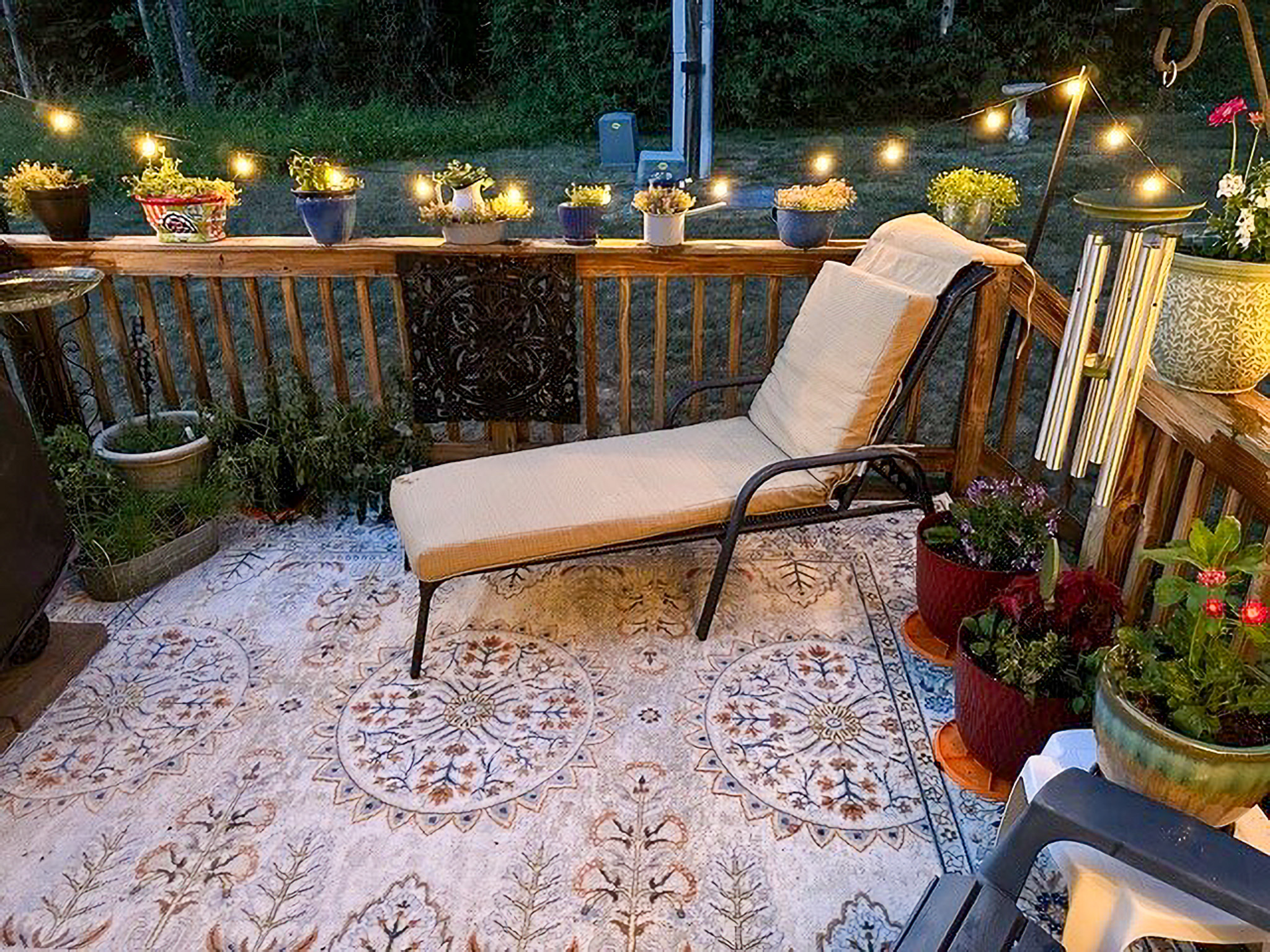 Cozy deck at dusk with string lights, potted plants, and a cushioned lounge chair on a patterned outdoor rug at the home of Sponsored Residential Providers Nancy and Zach Kaplan in Waynesboro, Virginia.
