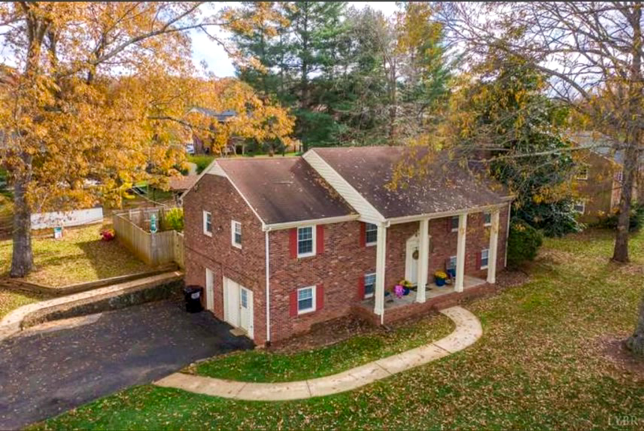 Aerial view of a brick two‑story house with white columns, surrounded by autumn trees and a curved walkway belonging to Sponsored Residential Providers Takeyshia Gibson and Antonio Carter in Forest, Virginia.