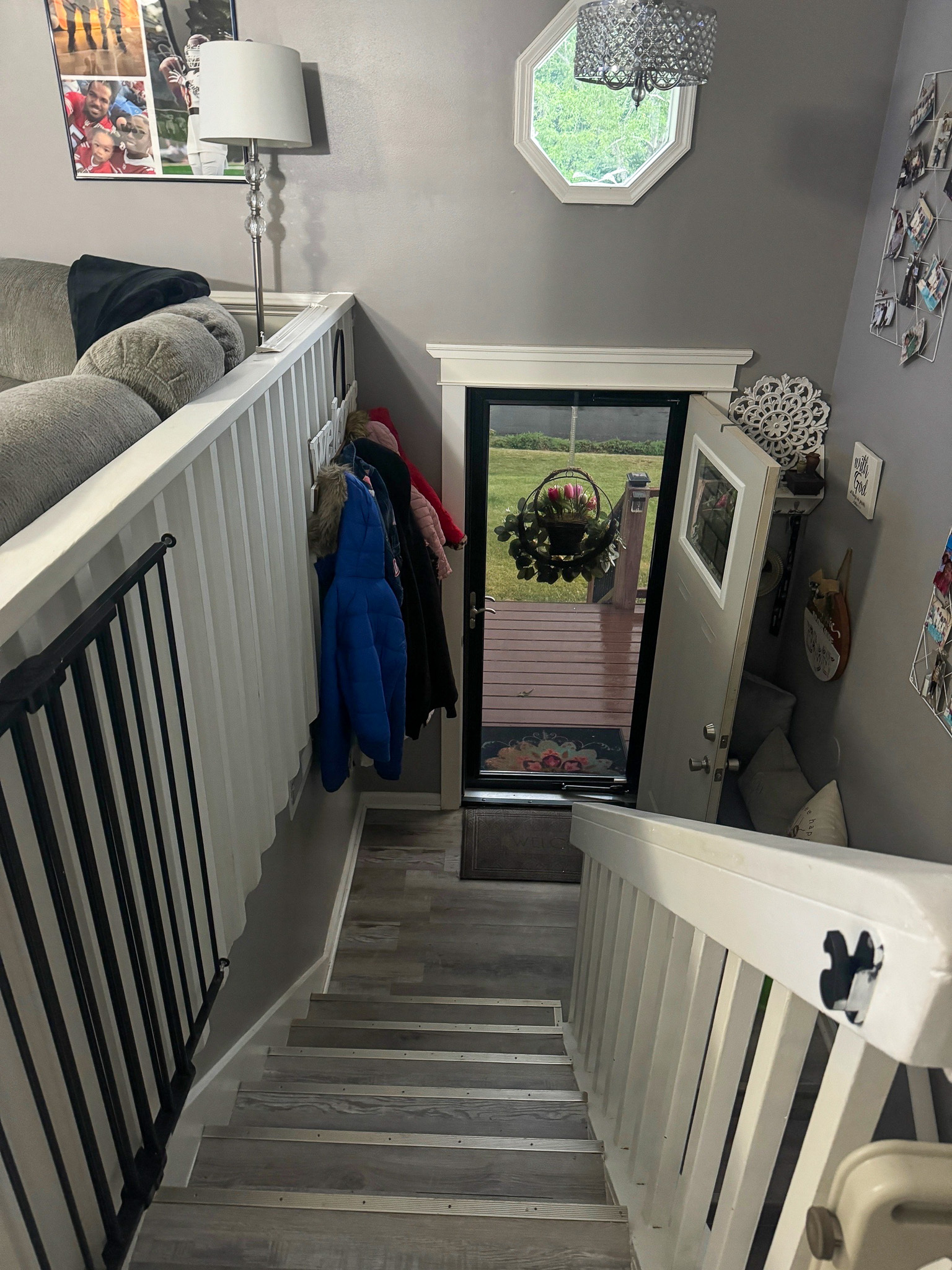 Stairway with white railings leading down to a glass front door decorated with a wreath, with coats hanging on hooks and a small window above inside the home of Sponsored Residential Providers Anthony Barnes and Demita Taylor in Forest, Virginia.