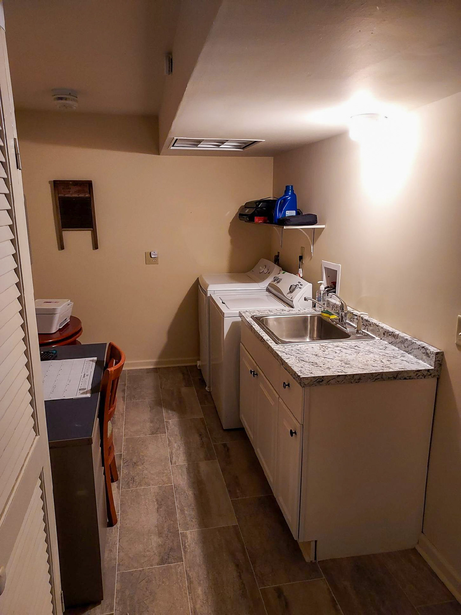 Laundry room with a washer, dryer, utility sink, countertop, and overhead shelving along a narrow hallway inside the home of Sponsored Residential Provider David Wilcox in Harrisonburg, Virginia.