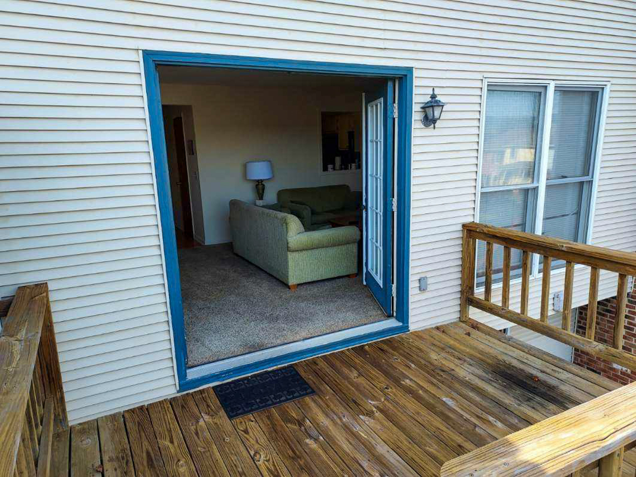 Wooden deck outside a home with open French doors leading into a living room furnished with a green sofa and lamp at the home of Sponsored Residential Provider David Wilcox in Harrisonburg, Virginia.