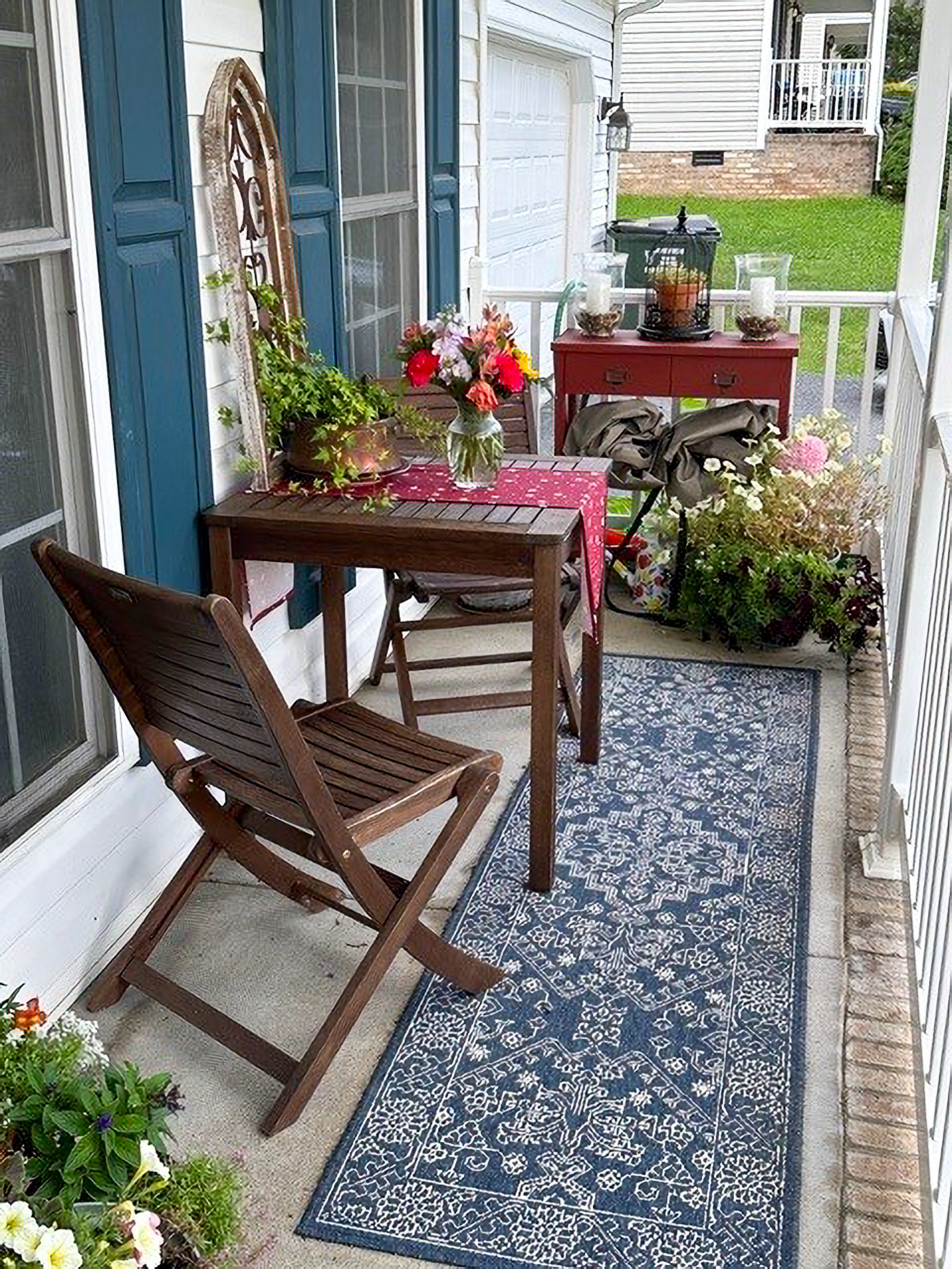 Small front porch with a wooden table and chairs, potted plants, a patterned rug, and flowers arranged on a side table at the home of Sponsored Residential Providers Nancy and Zach Kaplan in Waynesboro, Virginia.