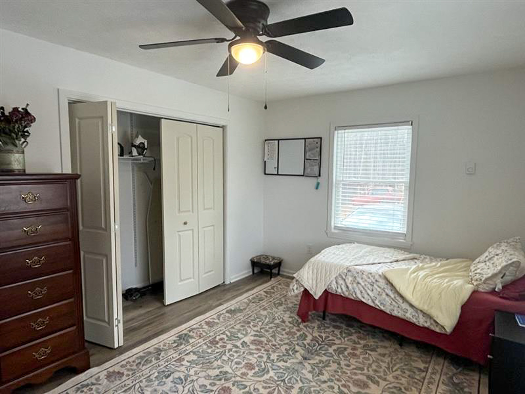 Bedroom with bed, patterned rug, dresser, ceiling fan, window, and open closet inside the home of Sponsored Residential Provider Kristen Bowers in Galax, Virginia.