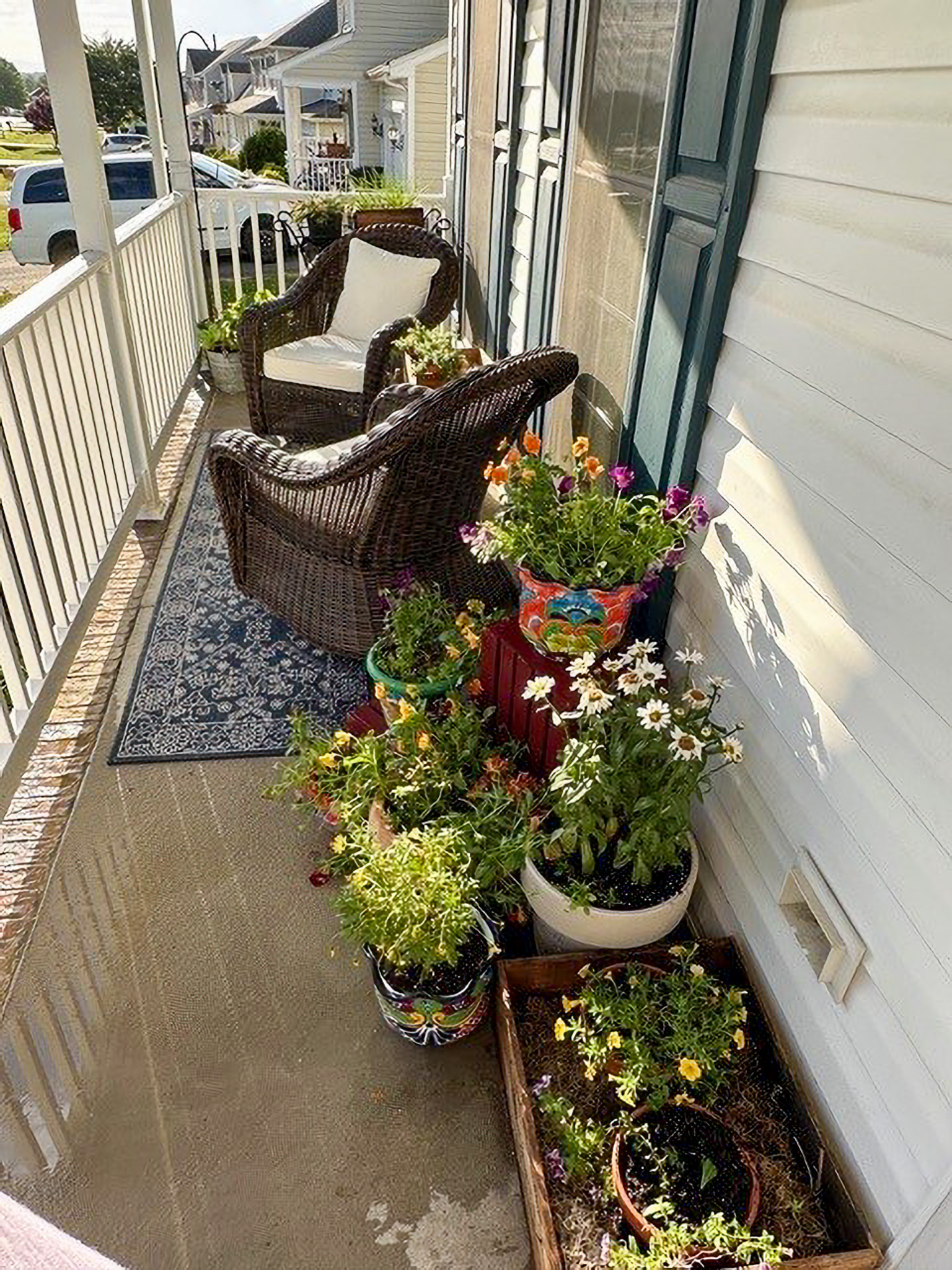 Front porch with wicker chairs, a patterned rug, and many colorful potted flowers along the railing at the home of Sponsored Residential Providers Nancy and Zach Kaplan in Waynesboro, Virginia.