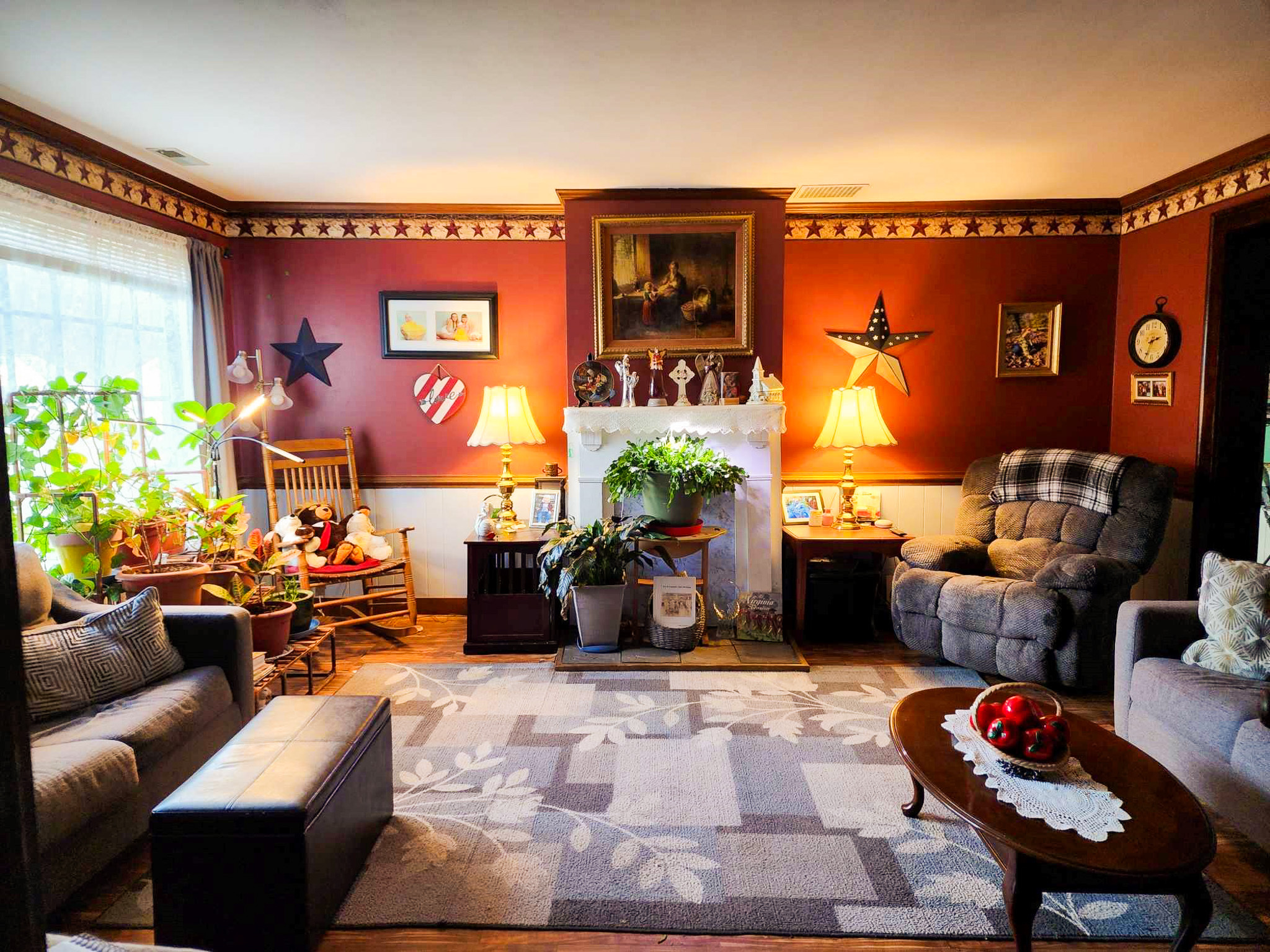 Cozy living room with deep red walls, a fireplace surrounded by plants, two armchairs, a sofa, and decorative stars on the walls Sponsored Residential Provider Angela Justice in Mathews, Virginia.