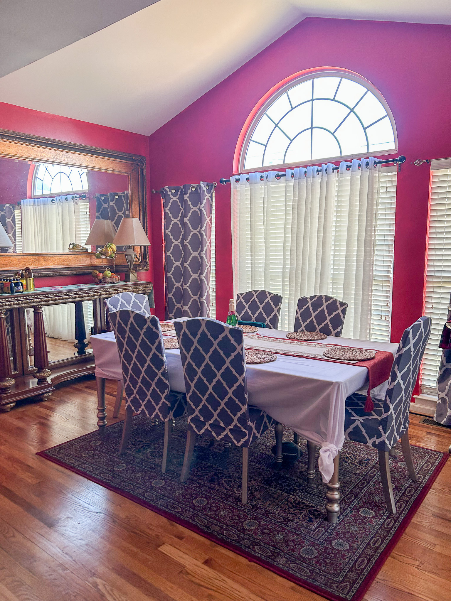 Dining room with red walls, rectangular table, patterned chairs, area rug, and large arched window inside the home of Sponsored Residential Provider Aidah Brassier in Spotsylvania, VA.