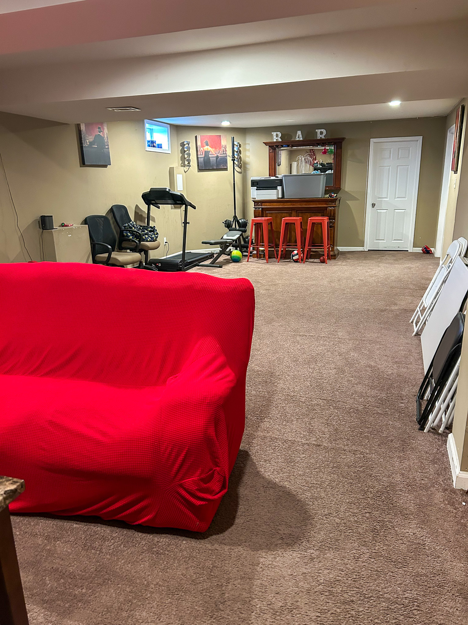 Finished basement with carpeted floor, red-covered seating, exercise equipment, and a small bar area inside the home of Sponsored Residential Provider Aidah Brassier in Spotsylvania, VA.