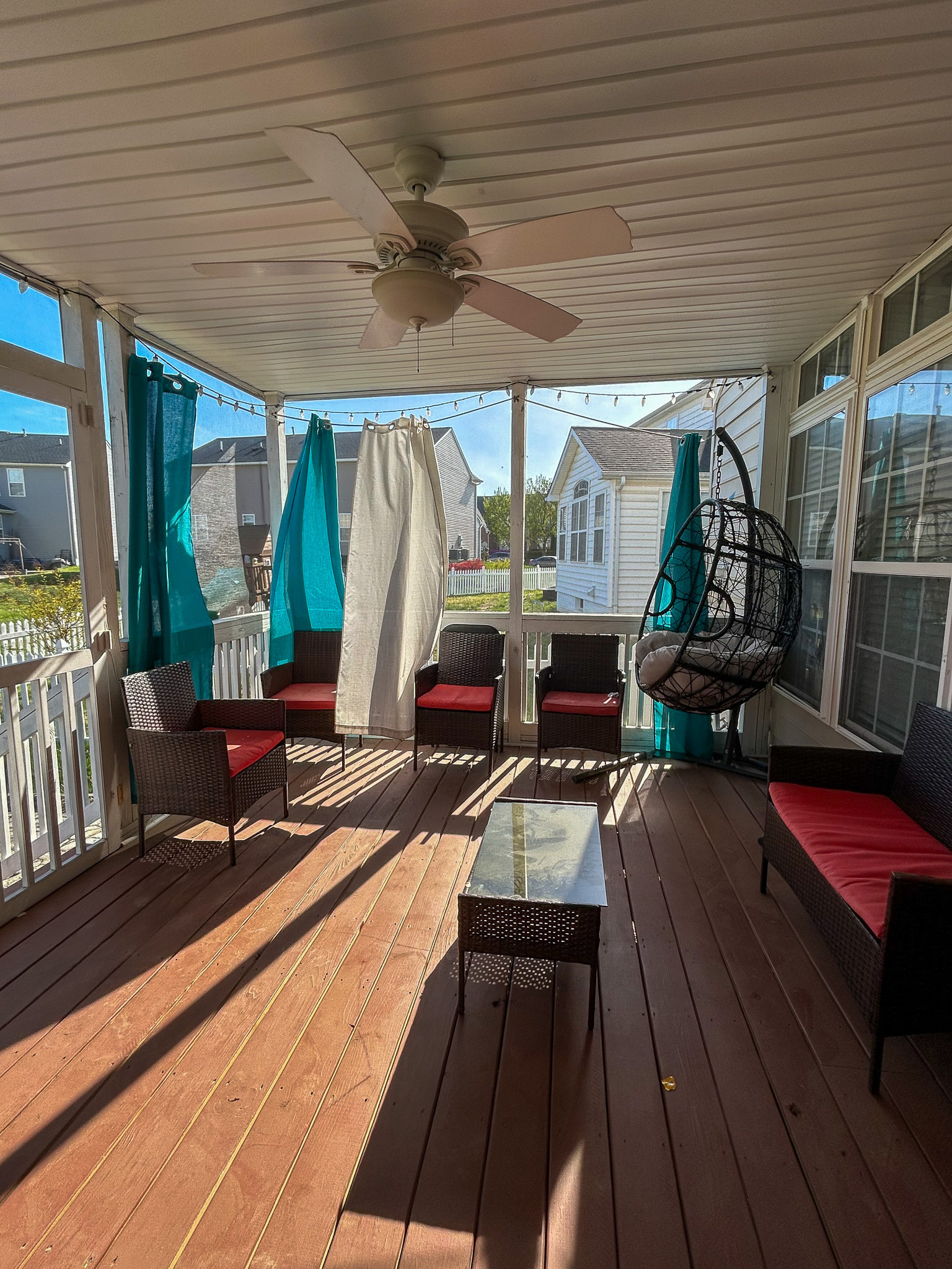 Screened porch with outdoor seating, ceiling fan, hanging chair, and wooden deck flooring inside the home of Sponsored Residential Provider Aidah Brassier in Spotsylvania, VA.