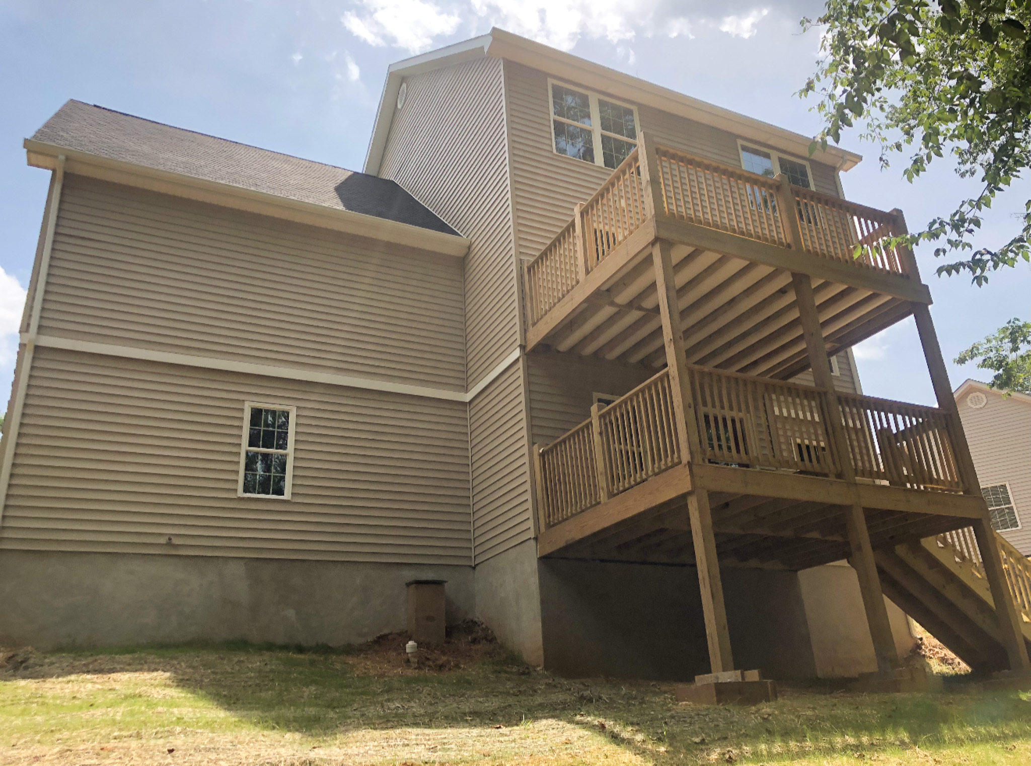 Rear view of a house with tan siding and two stacked wooden decks supported by posts, overlooking a sloped yard belonging to Sponsored Residential Providers Tonya and Michael Stewart in Lynchburg, Virginia.