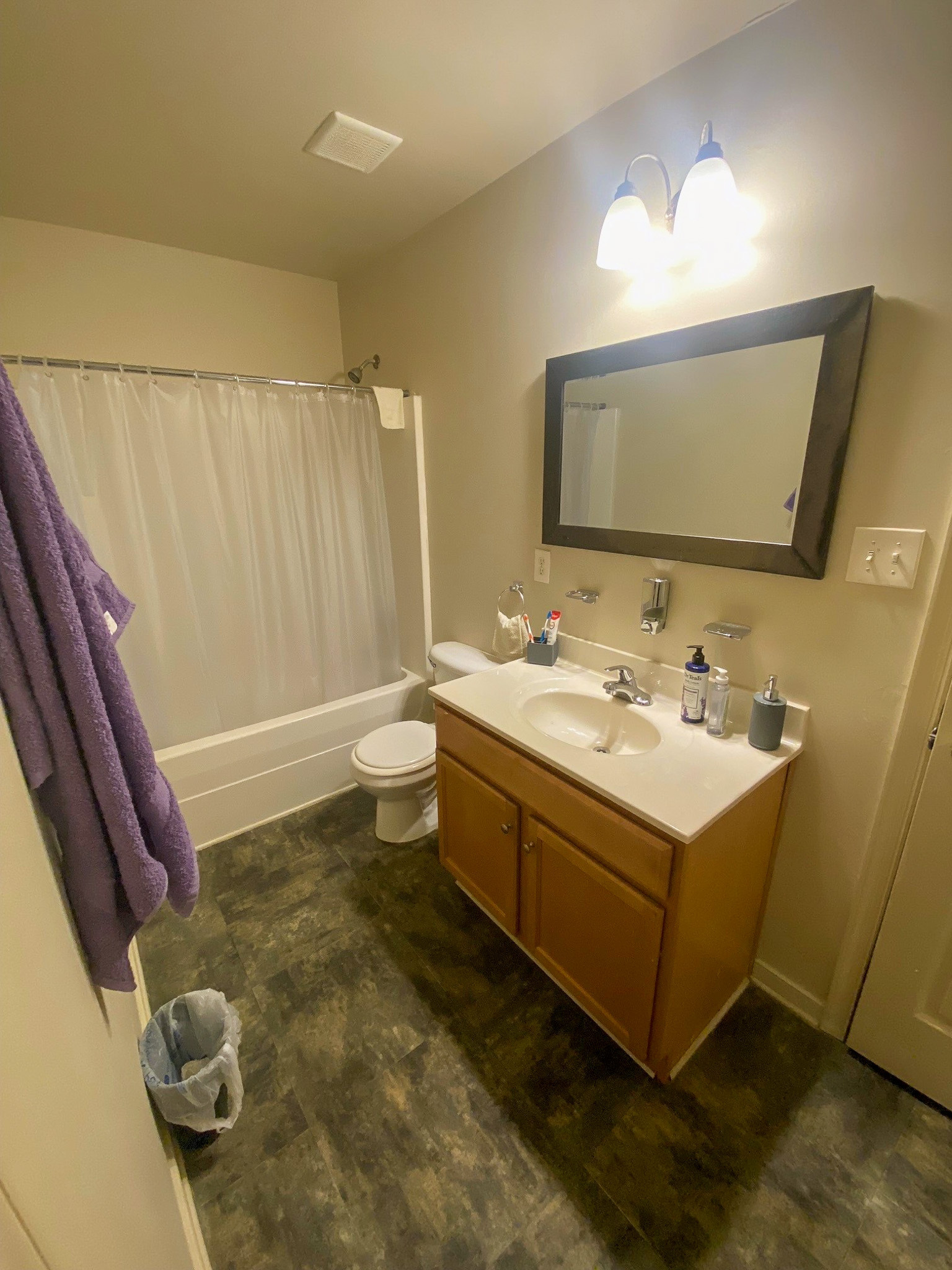 A bathroom with a single-sink vanity, large mirror, toilet, and a shower‑tub combo with a white curtain inside the home of Sponsored Residential Providers Xaiver Heath and David Williams in Richmond, Virginia.