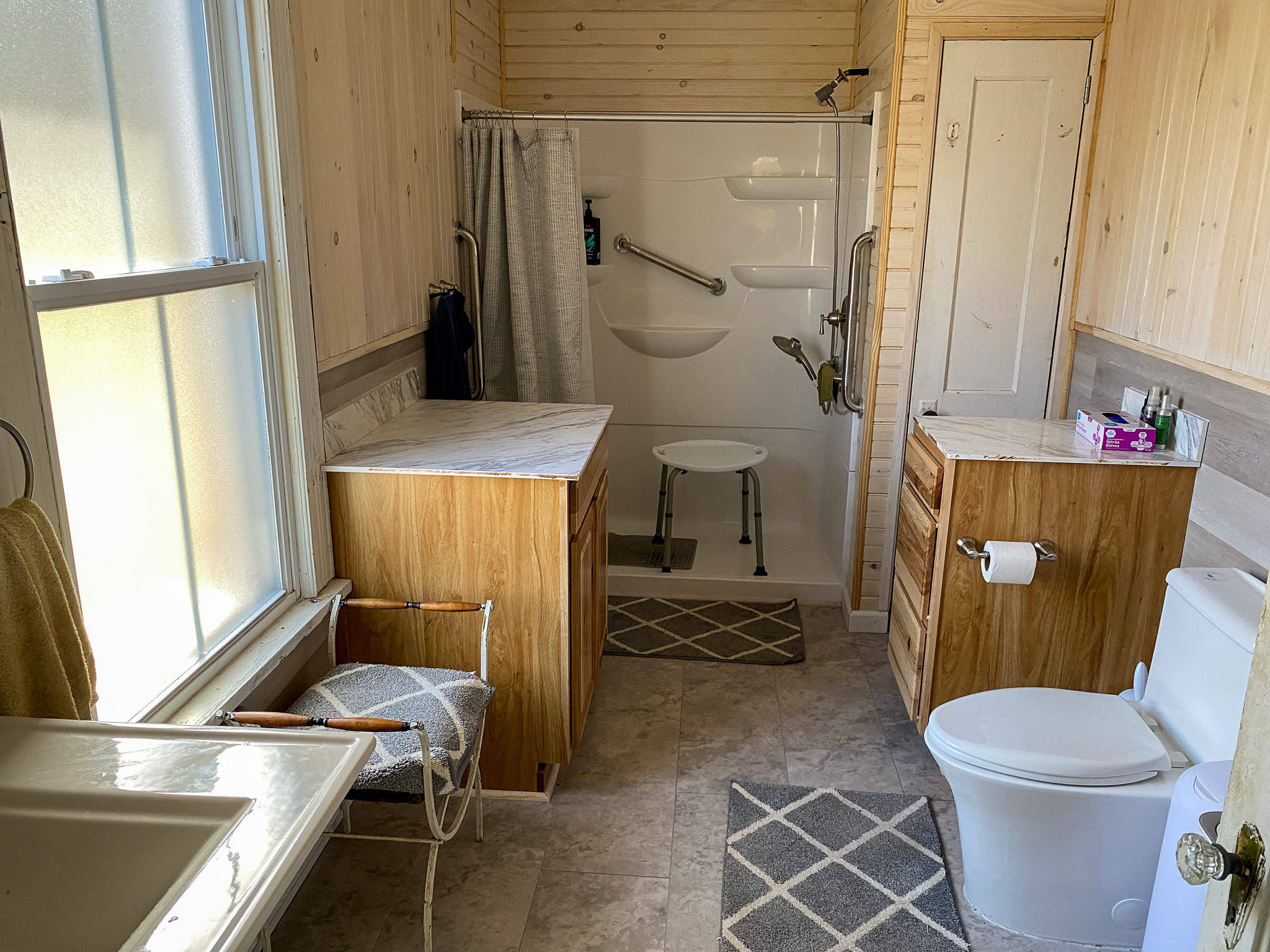 Accessible bathroom with walk-in shower, grab bars, shower chair, wood cabinets, and toilet inside the home of Sponsored Residential Providers Barbara and Larry Hatcher in Floyd, Virginia.