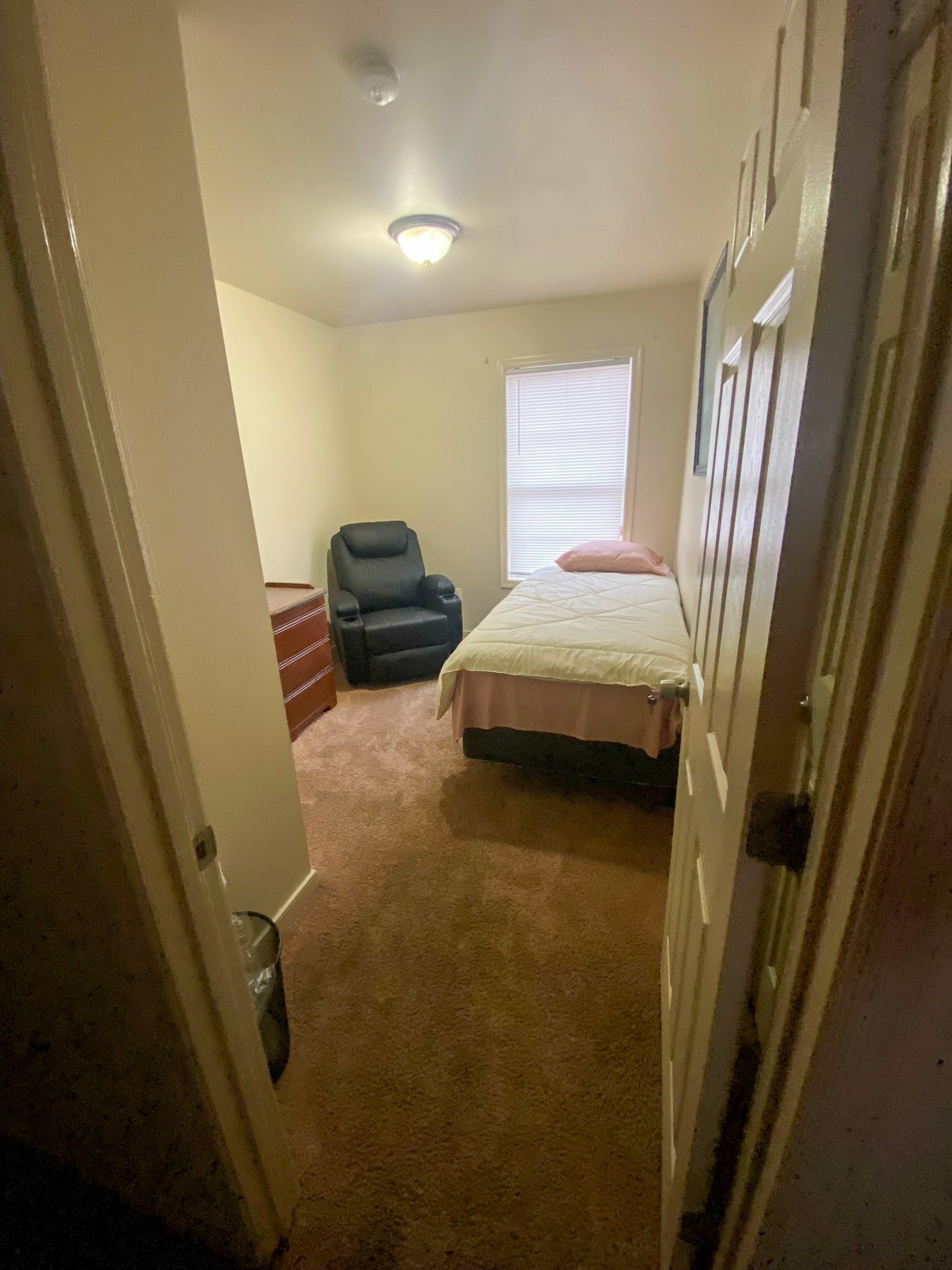 A small bedroom with a single bed, dresser, and cushioned chair arranged along the walls inside the home of Sponsored Residential Providers Xaiver Heath and David Williams in Richmond, Virginia.