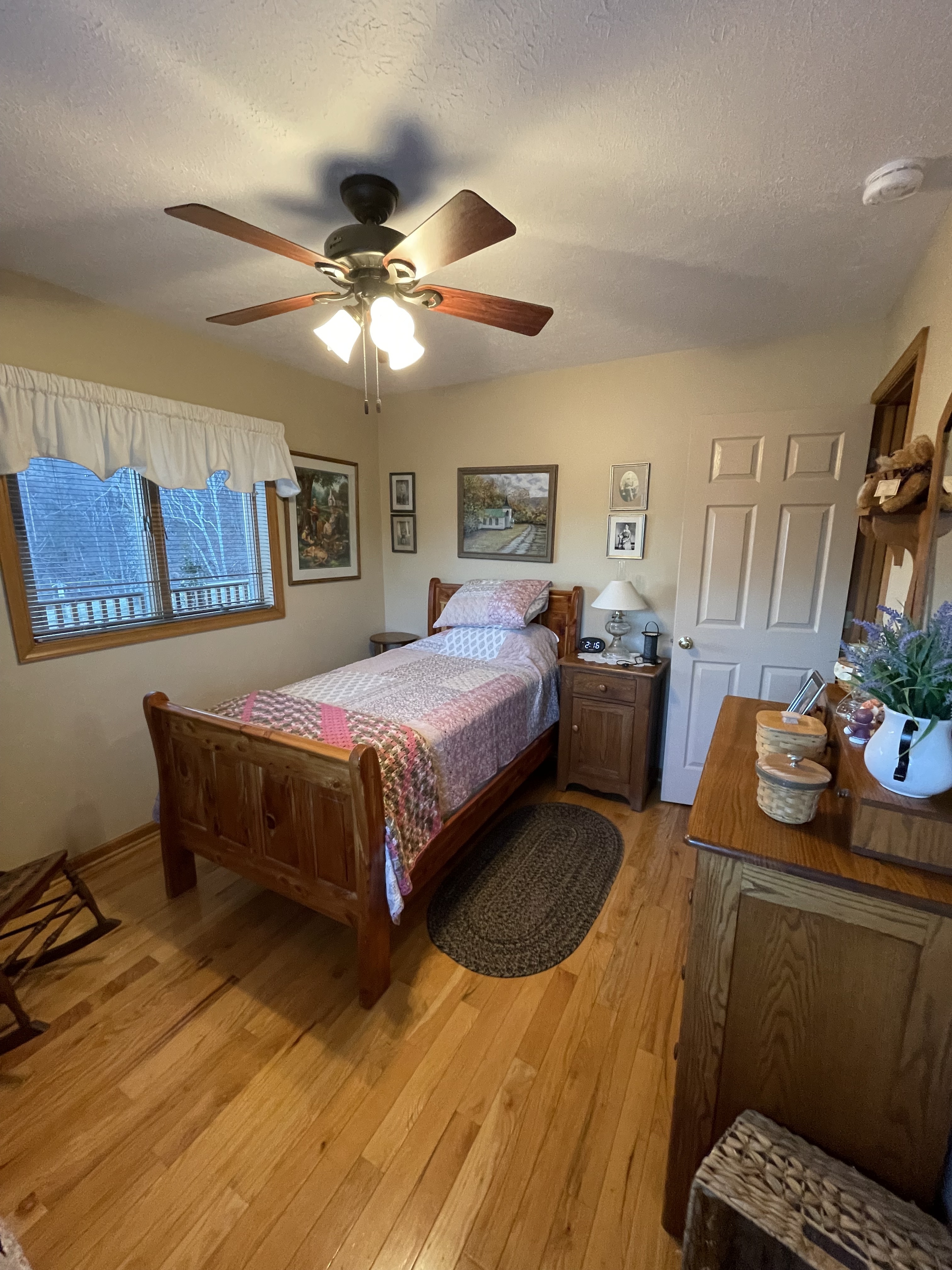 Small bedroom with a wooden twin bed, matching dresser, ceiling fan, framed wall art, and hardwood floors inside the home of Sponsored Residential Providers Jimmy and Nancy Ayers in Monroe, Virginia.