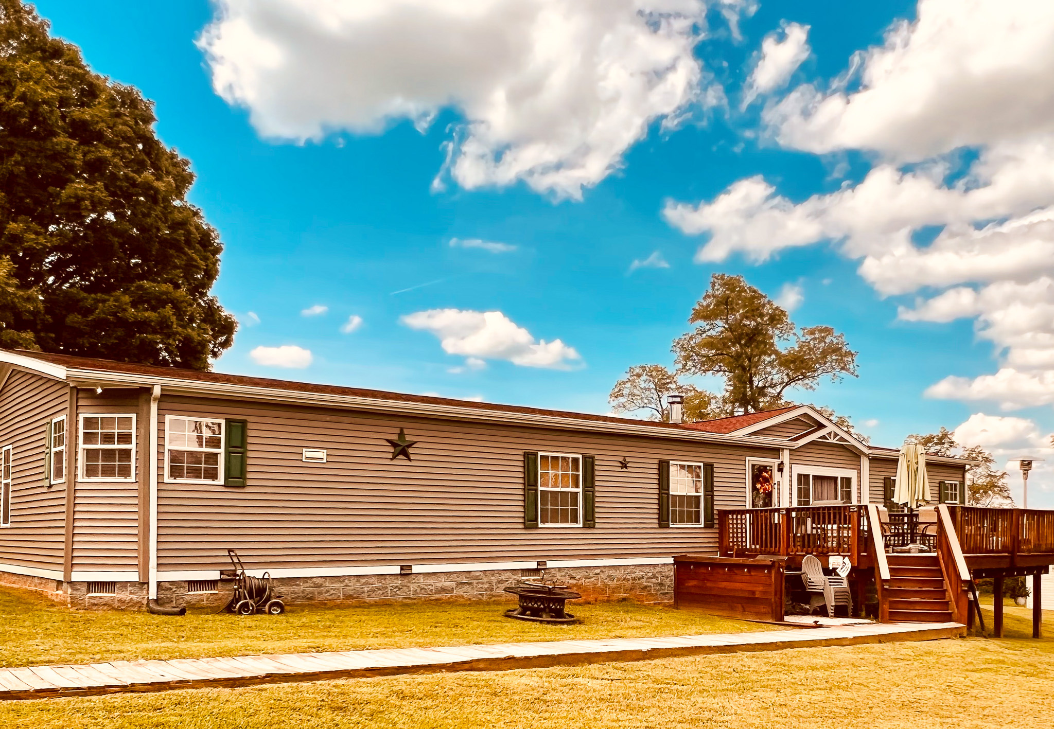 A long single‑story manufactured home with a small front deck and outdoor seating in a grassy yard belonging to Group Home Providers Cory and Jessica Berger in Bedford County, Virginia.
