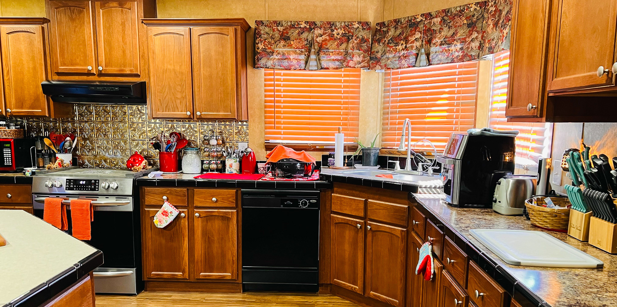 A kitchen with wooden cabinets, a stove, a dishwasher, and countertops filled with small appliances and utensils inside the home of Group Home Providers Cory and Jessica Berger in Bedford County, Virginia.