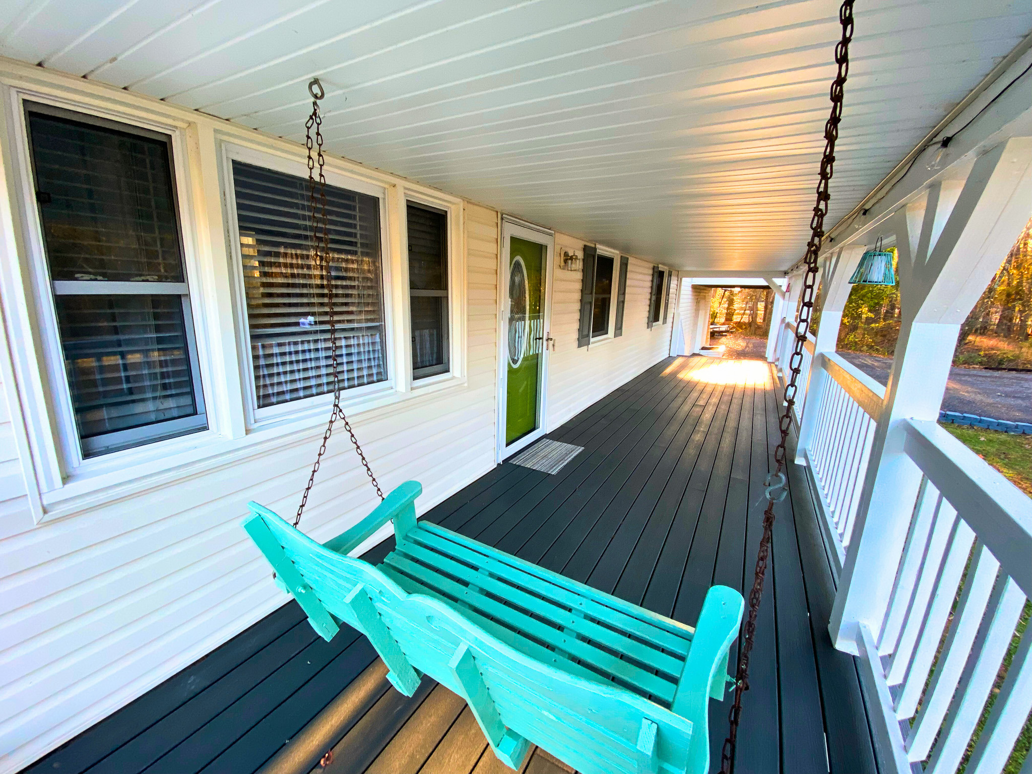 Long covered front porch with white siding, multiple windows, a hanging turquoise bench swing, and dark flooring extending along the exterior of home belonging to Sponsored Residential Providers Bradley and Andrea Smith in Richmond.