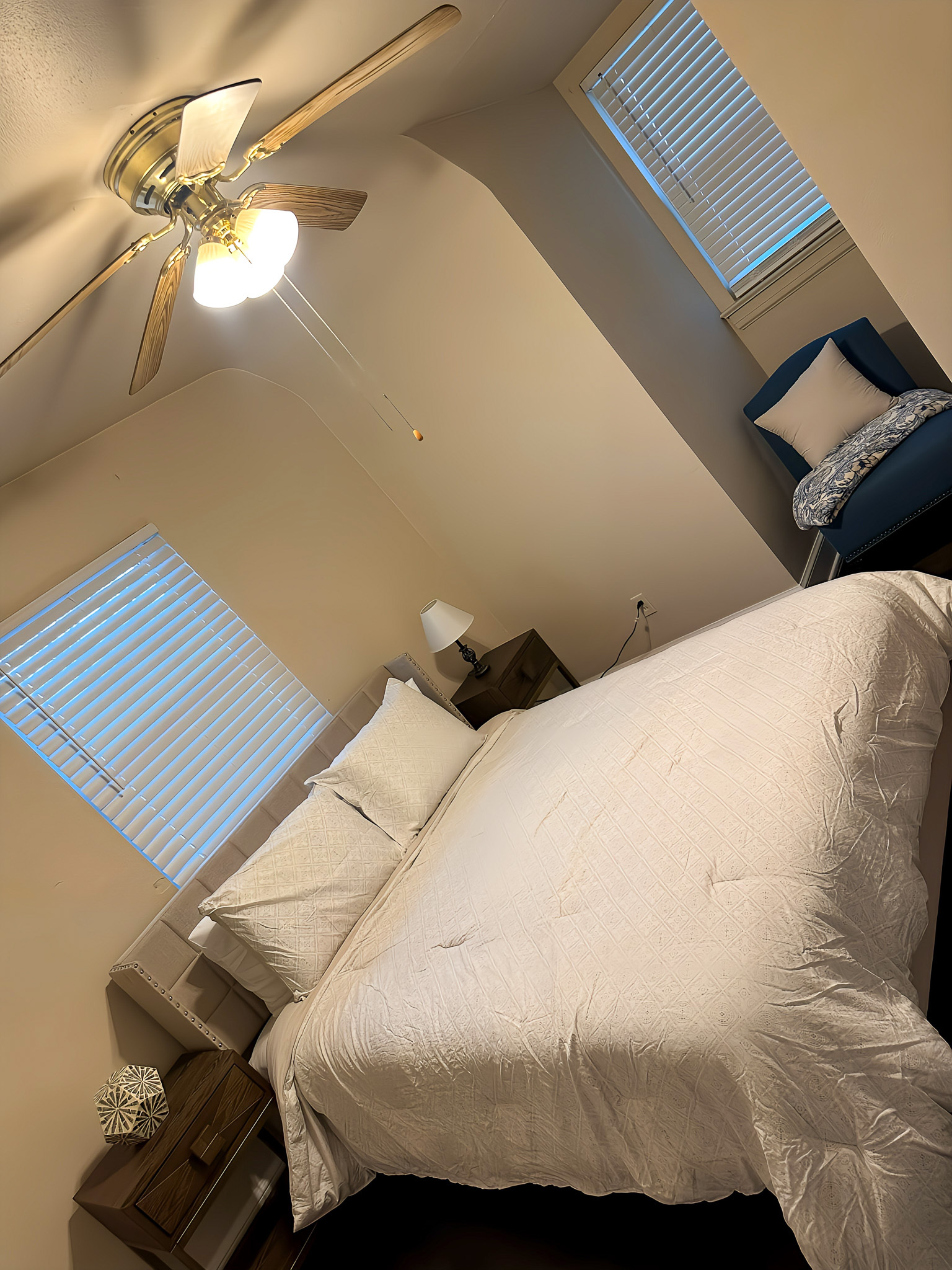 A bedroom with a large neatly made bed, two nightstands, and a small seating area near the two window inside the home of Sponsored Residential Providers Gia & Celia Calloway in Roanoke, Virginia.