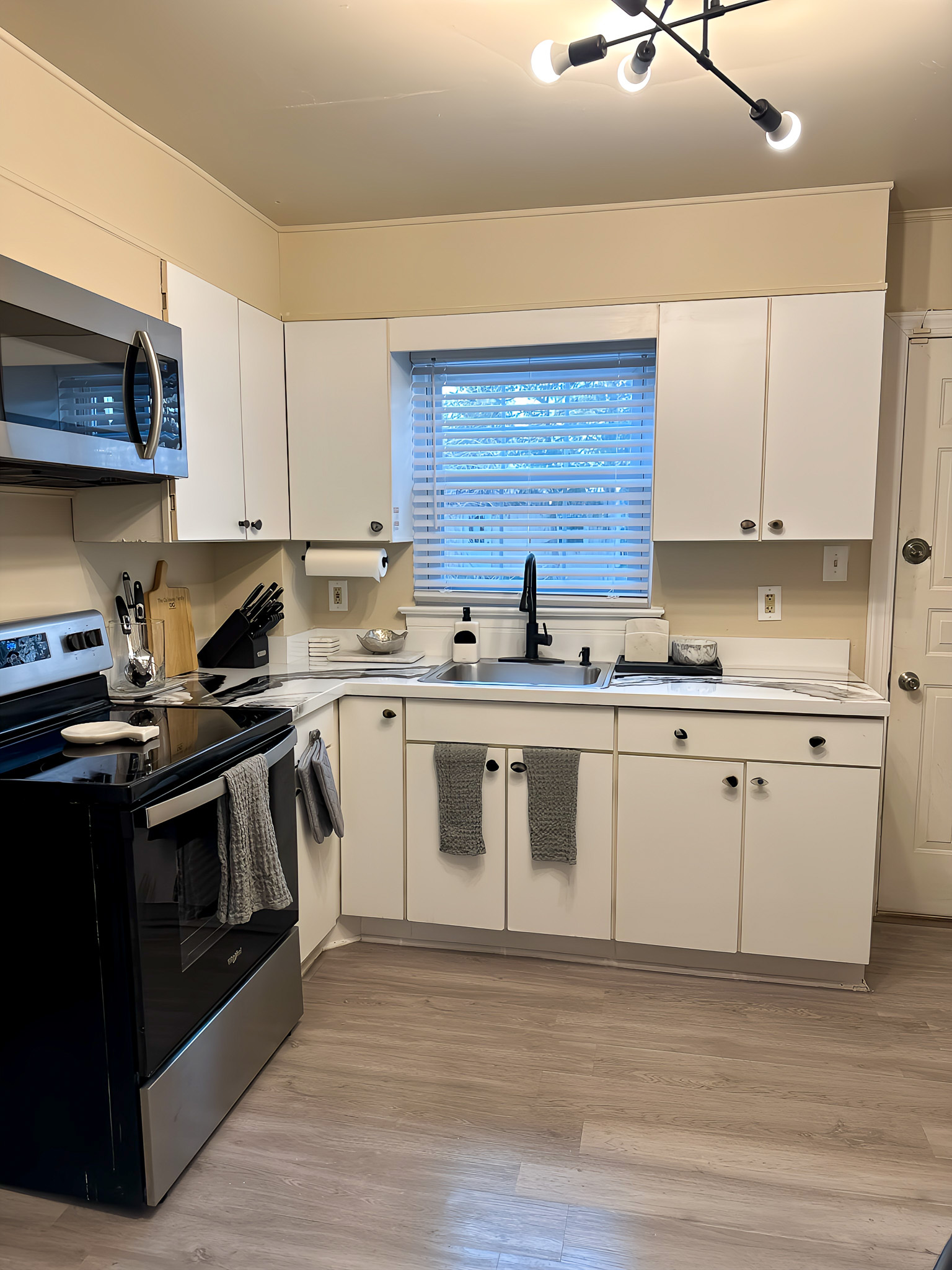 A small kitchen with white cabinets, a stainless steel stove and microwave, and a sink beneath a window inside the home of Sponsored Residential Providers Gia & Celia Calloway in Roanoke, Virginia.