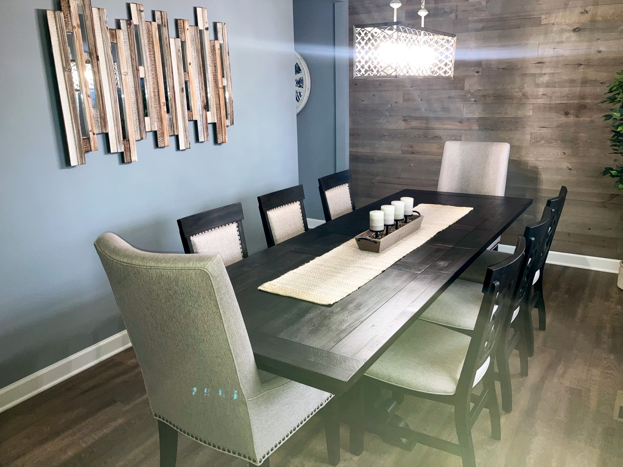 Modern dining room with a long dark table, upholstered chairs, a candle centerpiece, wall art, and a chandelier inside the home of Sponsored Residential Providers Crystal and Christopher Cameron in Fredericksburg, Virginia.