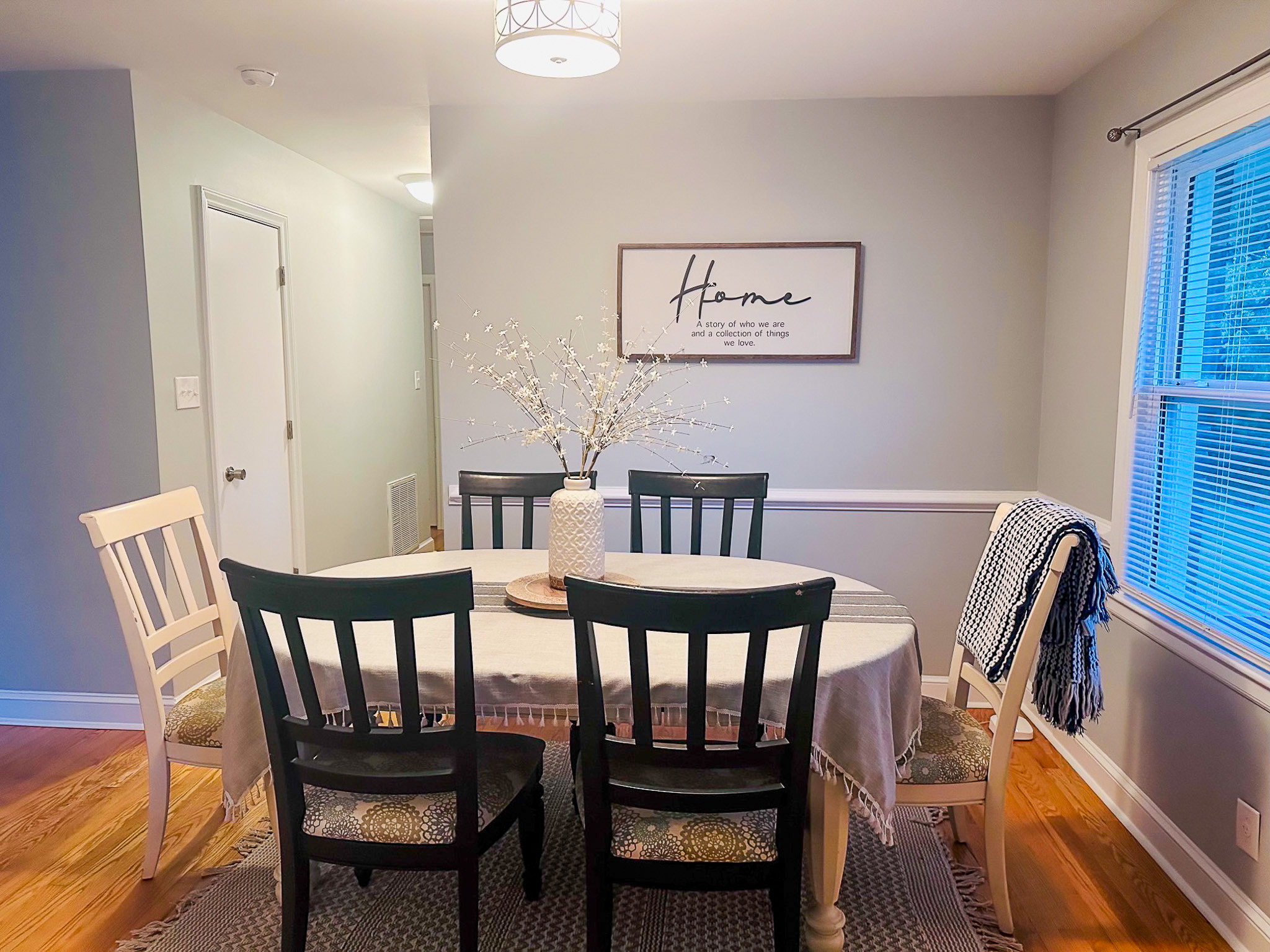 Dining area with table and mixed seating, decorative centerpiece, wall art, and window providing natural light inside the home of Sponsored Residential Providers Casey and Fred Doswell in Lynchburg, VA.