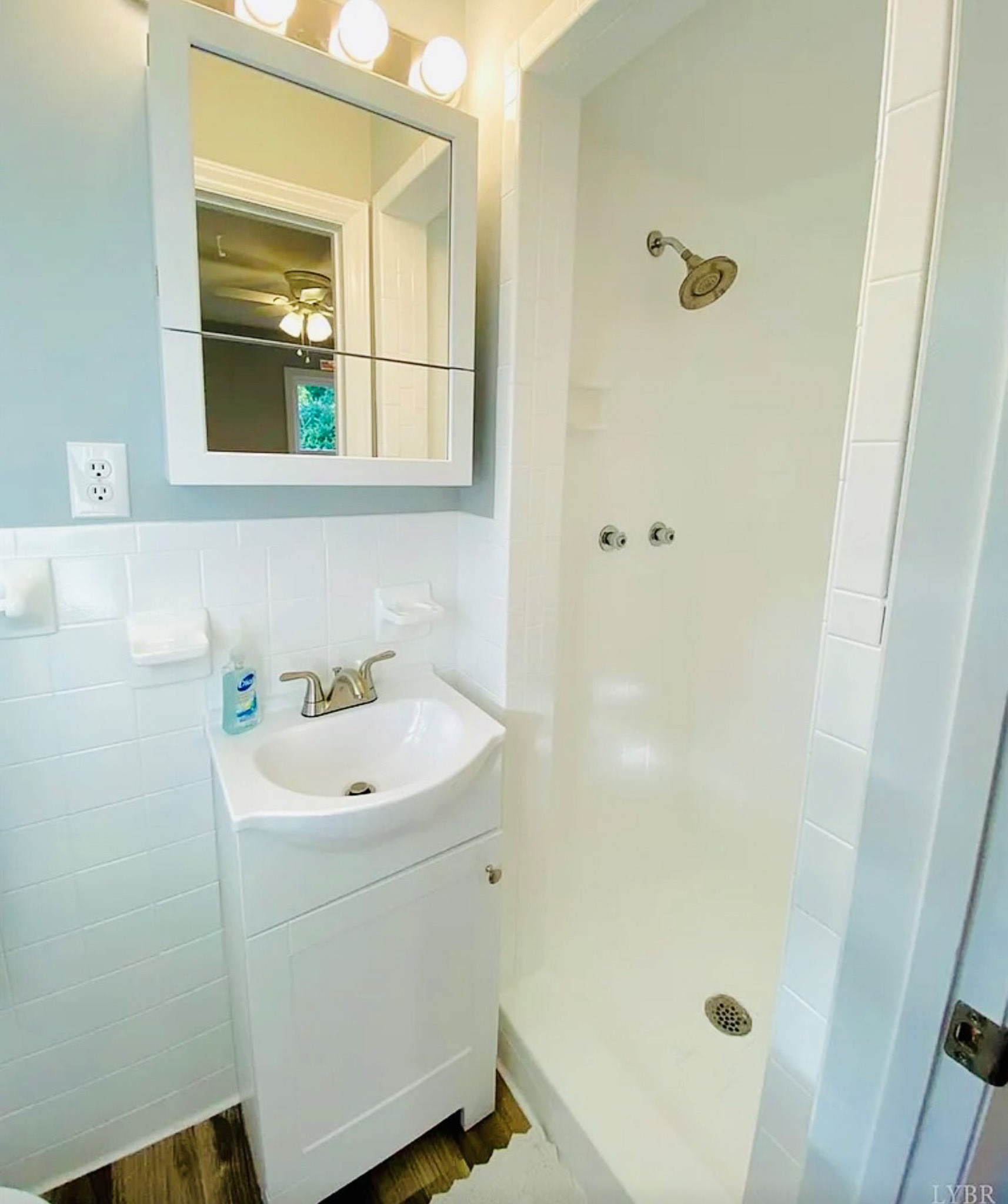 Bright bathroom with white vanity sink, wall mirror with lighting, and tiled walk-in shower with chrome fixtures inside the home of Sponsored Residential Providers Casey and Fred Doswell in Lynchburg, VA.