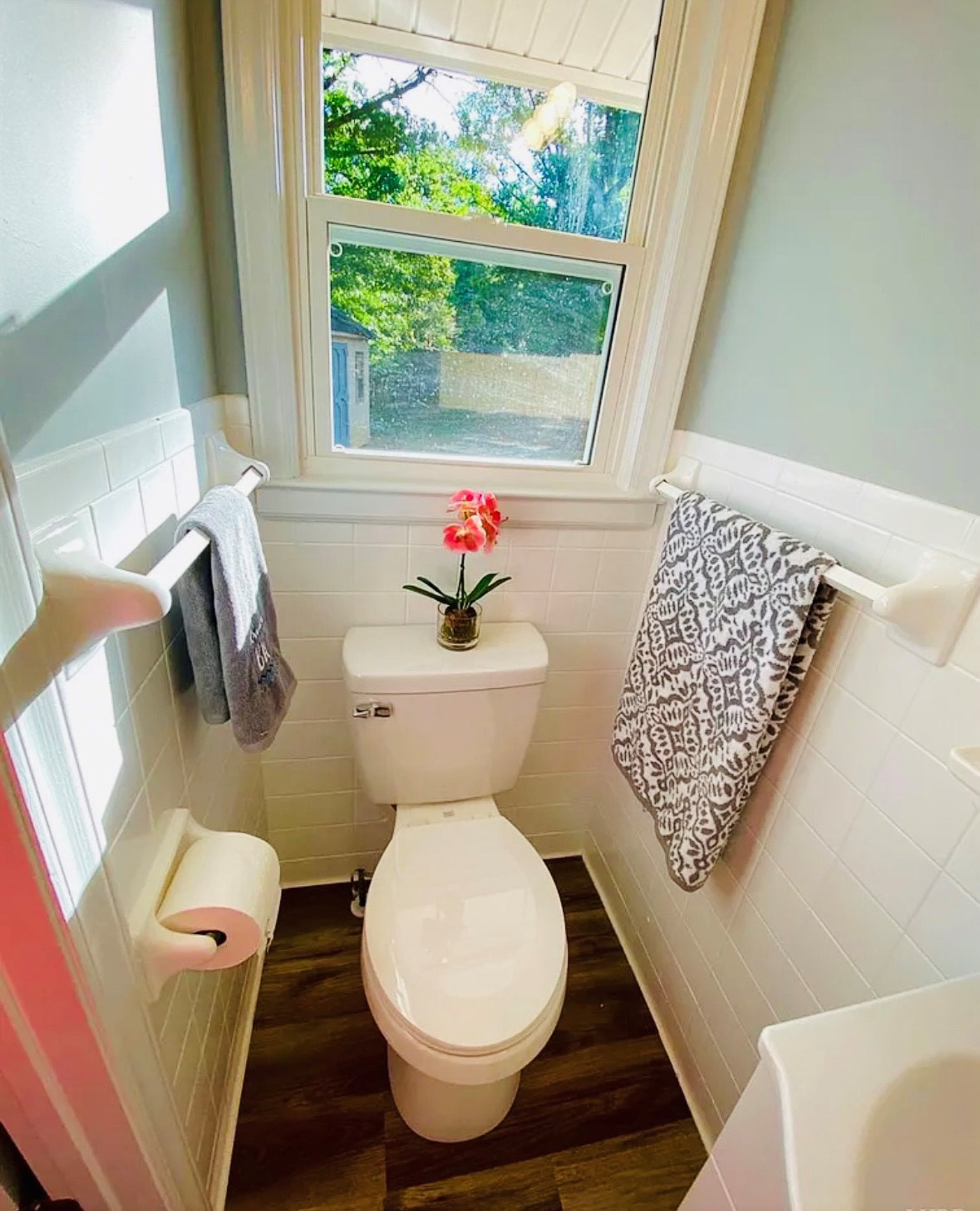 Bathroom with toilet beneath a window, white tile walls, towel racks, and natural light with outdoor view inside the home of Sponsored Residential Providers Casey and Fred Doswell in Lynchburg, VA.