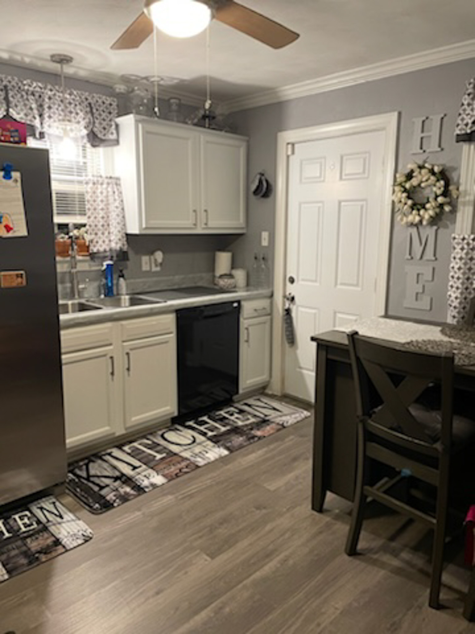 A kitchen with white cabinets, a stainless steel refrigerator, dark appliances, and a dining table positioned beside the back door  inside the home of Sponsored Residential Provider Claudia Davis in Roanoke, Virginia.