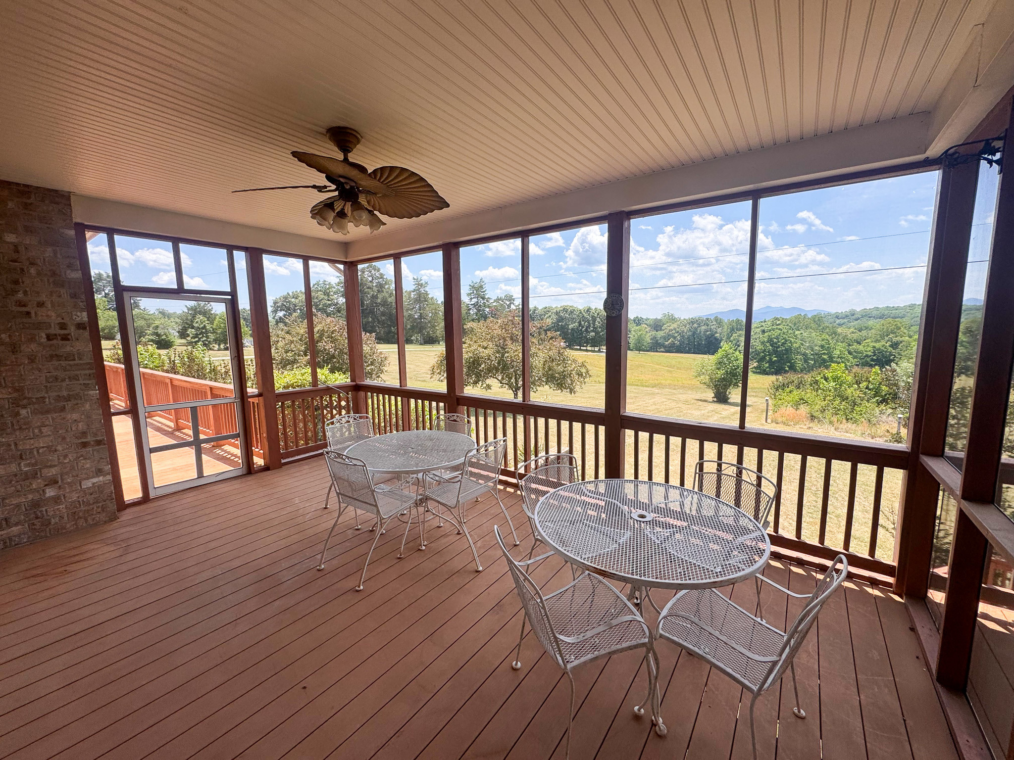 Covered screened-in porch with seating and round tables overlooking a wide yard and mountain views outside the home of Sponsored Residential Provider Clayton Lawson in Amherst, Virginia.
