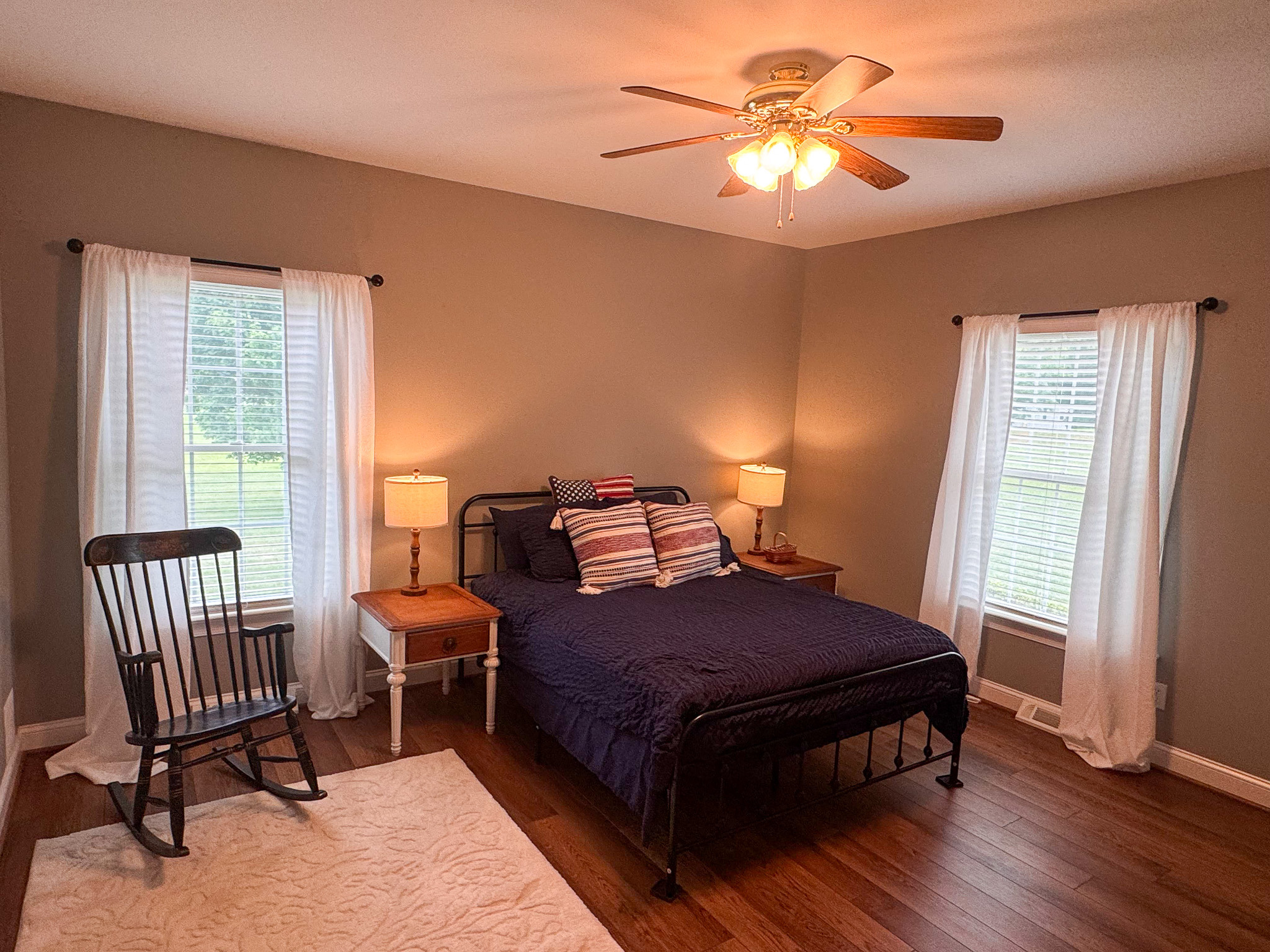 Bedroom with bed, windows with curtains, and rocking chair inside the home of Sponsored Residential Provider Clayton Lawson in Amherst, Virginia.
