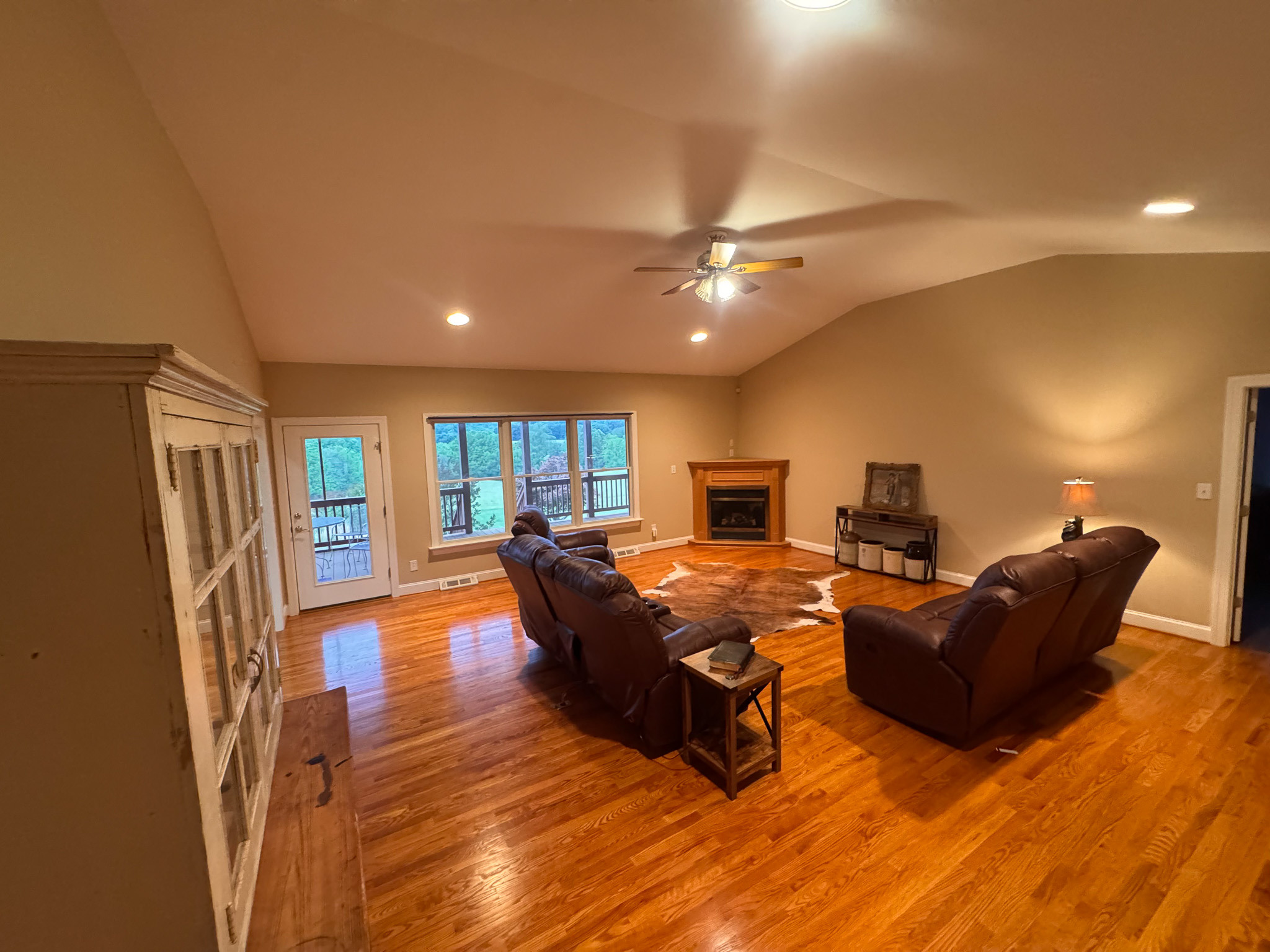 Living room with hardwood floors, leather seating, and large windows overlooking a wooded view inside the home of Sponsored Residential Provider Clayton Lawson in Amherst, Virginia.
