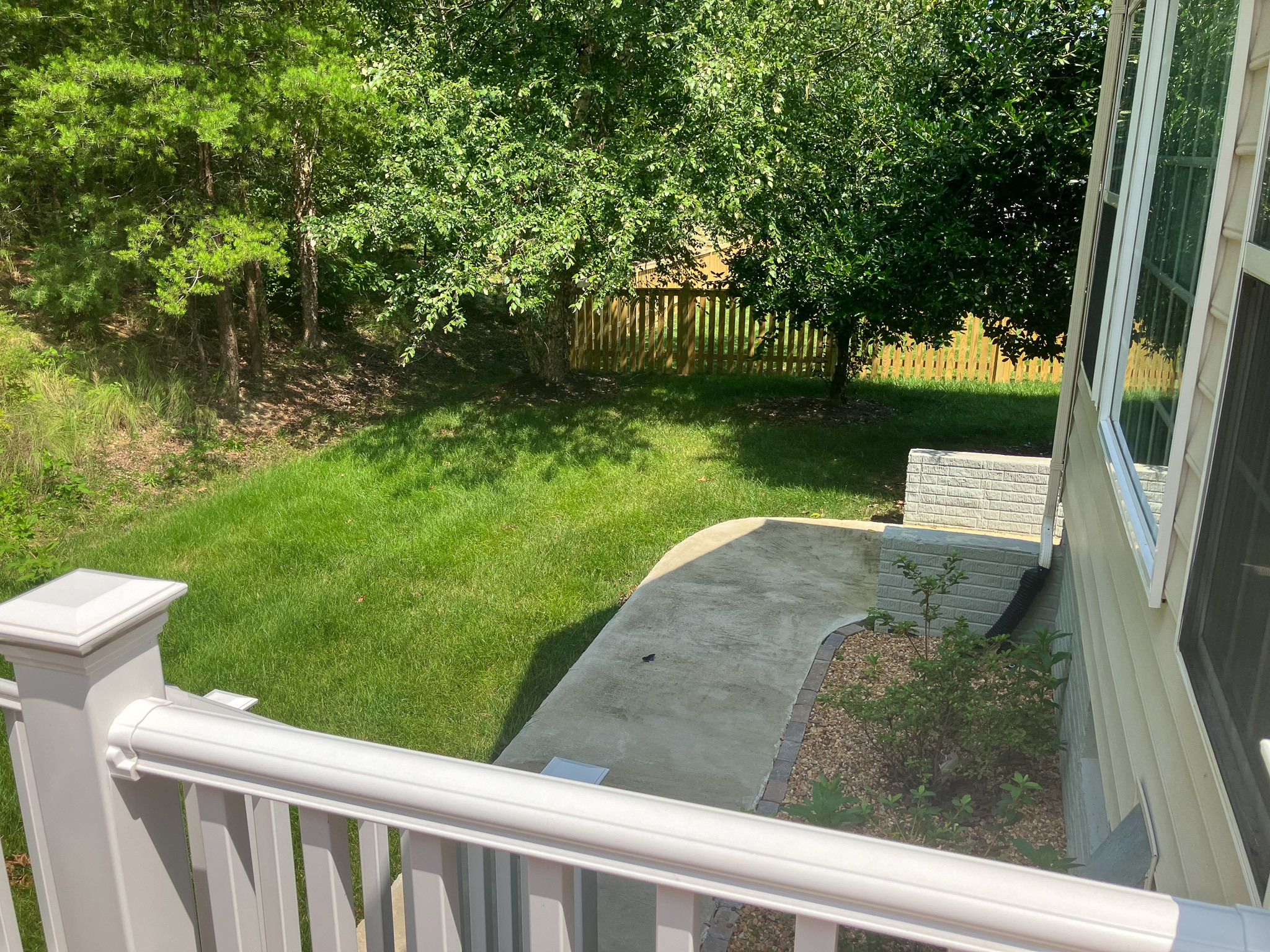 Green backyard with trees, grass, and a curved concrete walkway beside the house belonging to the Agency operated group home named Deep Creek in Fredericksburg, Virginia.