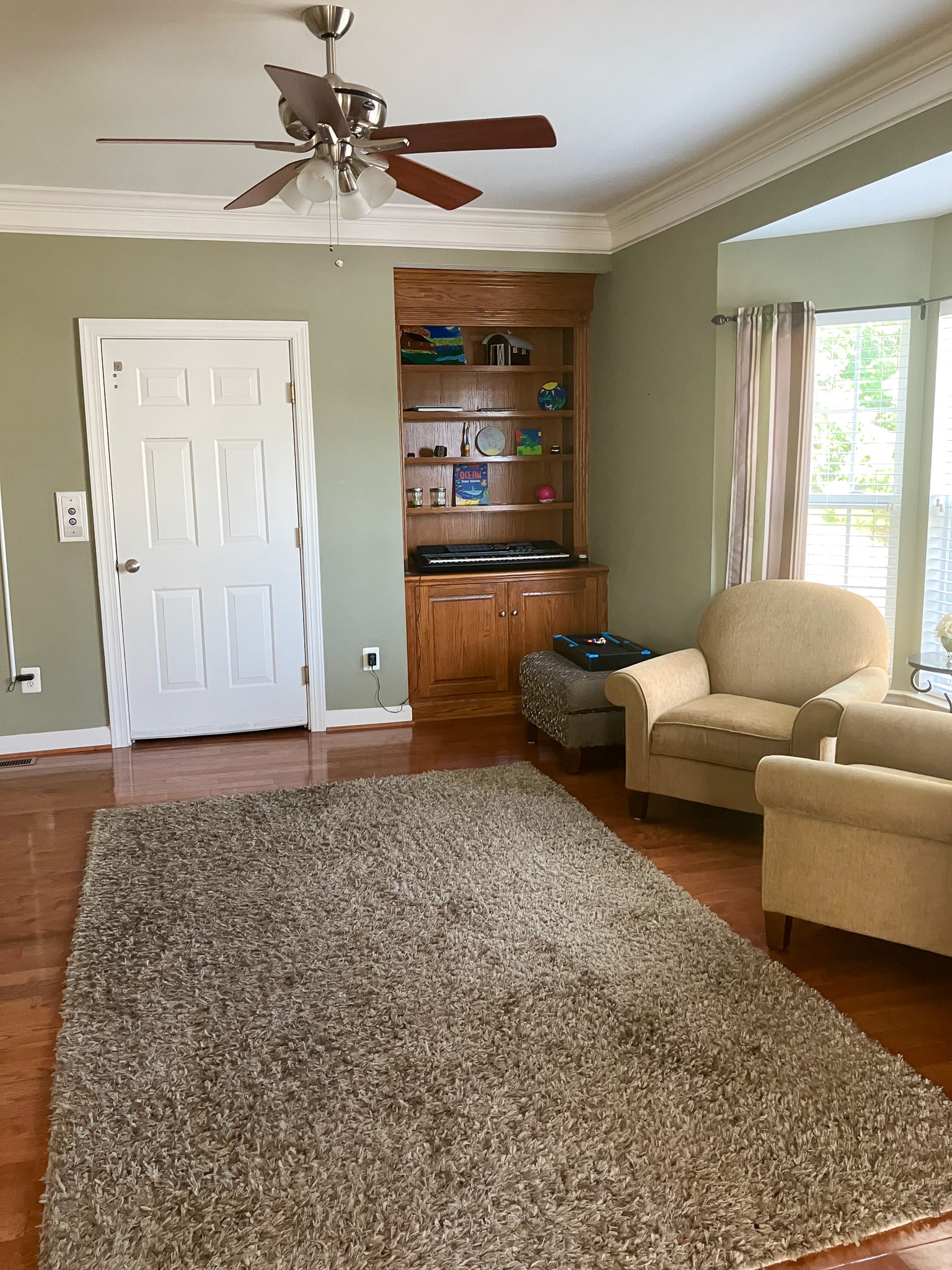 Cozy living room with armchairs, ceiling fan, built-in shelving, and hardwood floors belonging to the Agency operated group home named Deep Creek in Fredericksburg, Virginia.