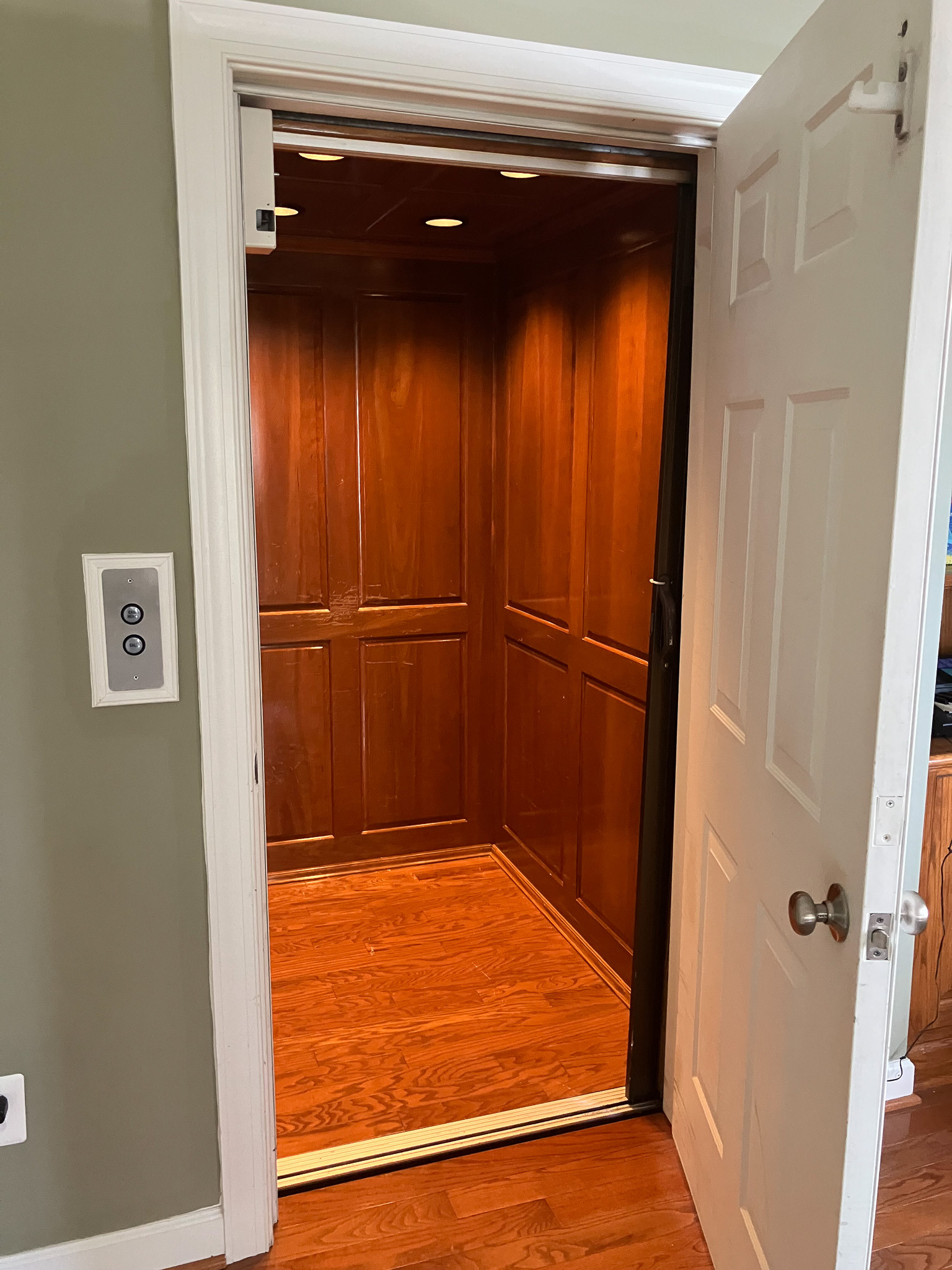 Residential elevator with wooden panel interior and wall-mounted call buttons, door open belonging to the Agency operated group home named Deep Creek in Fredericksburg, Virginia.