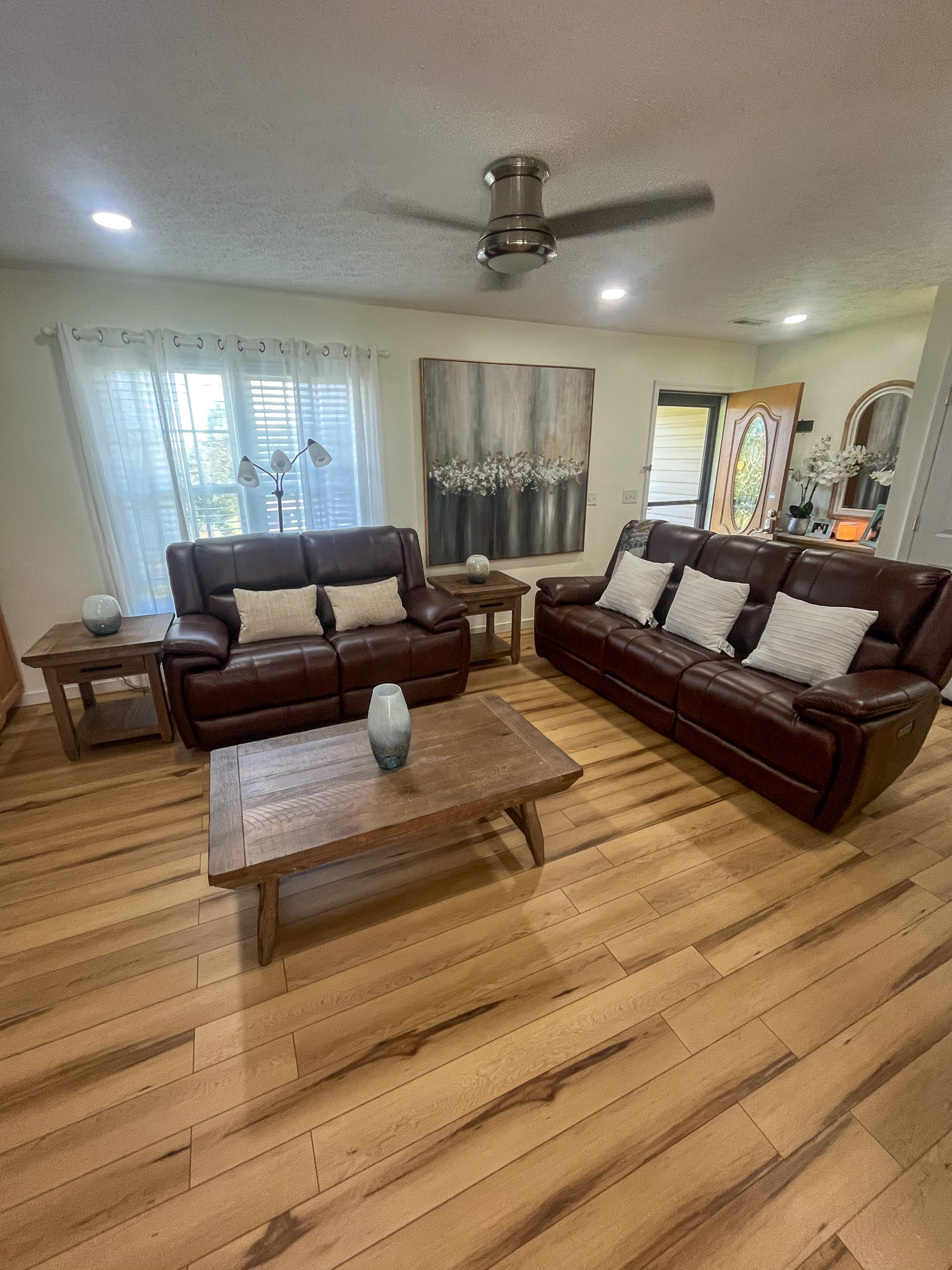 Bright, open living room with comfortable seating, wood flooring, large windows, and a welcoming entryway. This is the home of Sponsored Residential Provider Delmy Sexton in Woodlawn, VA.