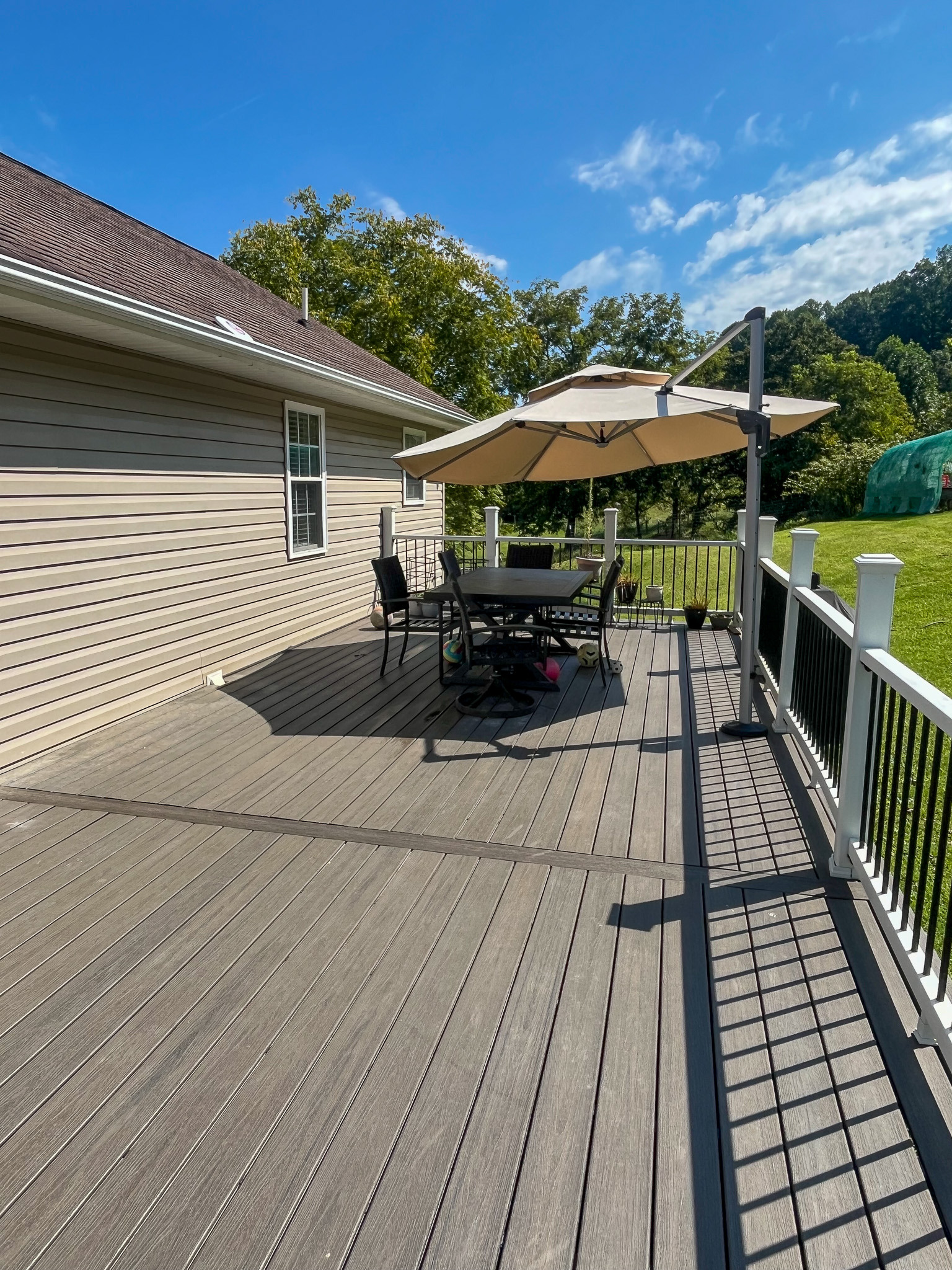 Accessible outdoor deck with railing, patio dining set, and umbrella overlooking a spacious yard. This is the home of Sponsored Residential Provider Delmy Sexton in Woodlawn, VA.