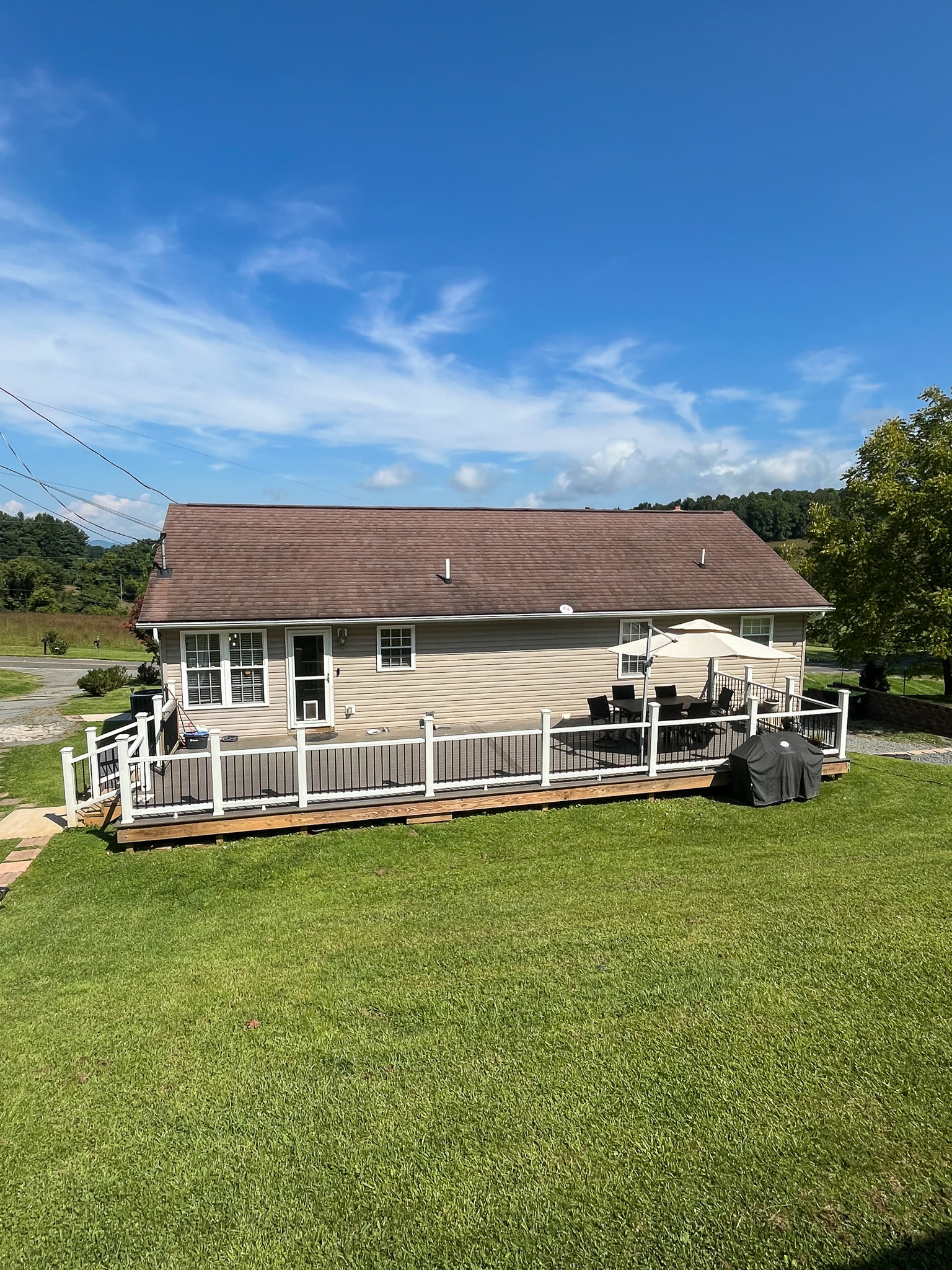 Rear view of the home featuring a large deck with outdoor seating, grilling area, and expansive grassy yard. This is the home of Sponsored Residential Provider Delmy Sexton in Woodlawn, VA.