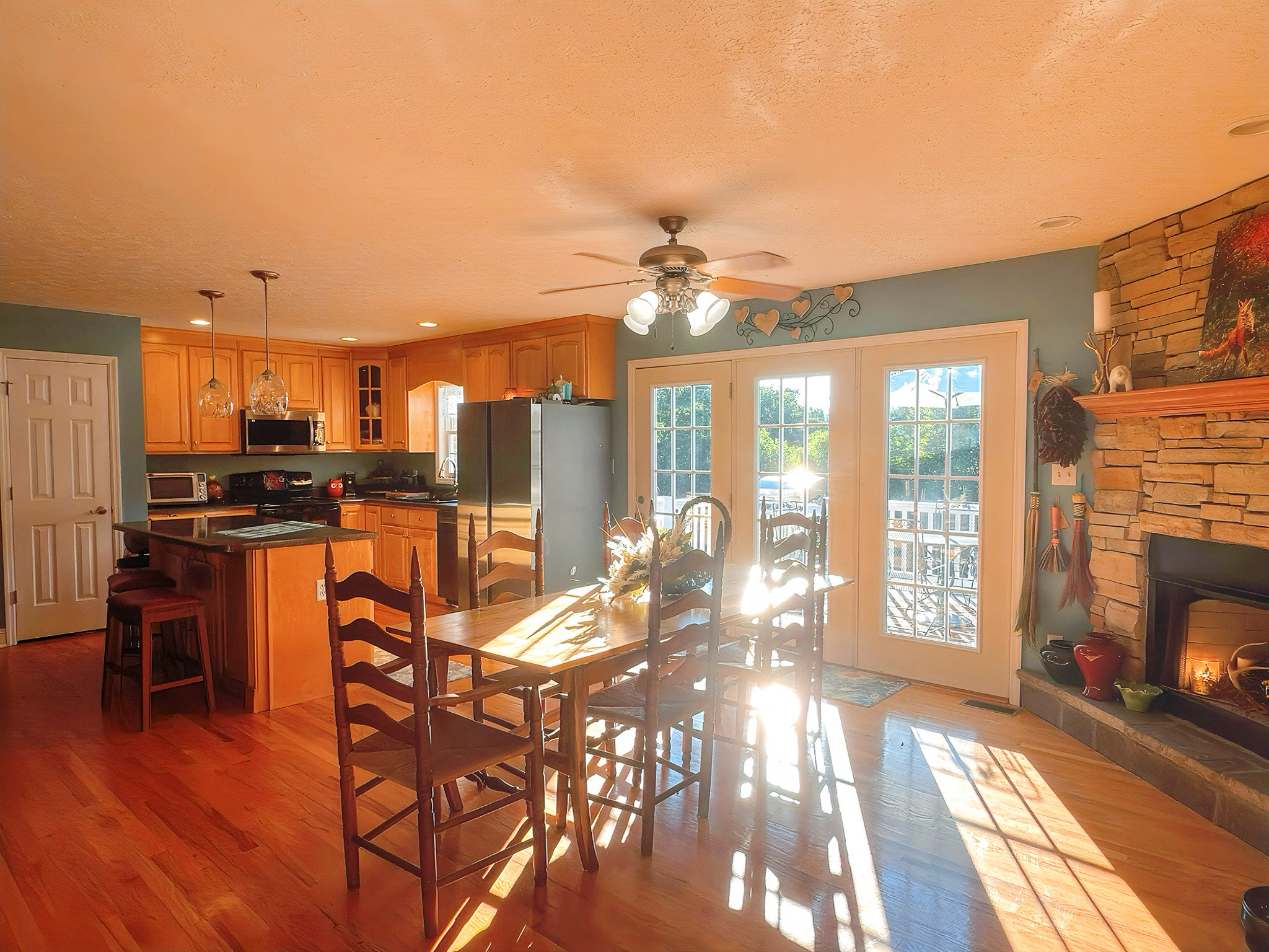 A kitchen and dining area with wood floors, wooden cabinets, a stone fireplace, and double doors opening to the outside in the home of Group Home Providers Kim and Rick Duncan in Patrick Springs, Virginia.