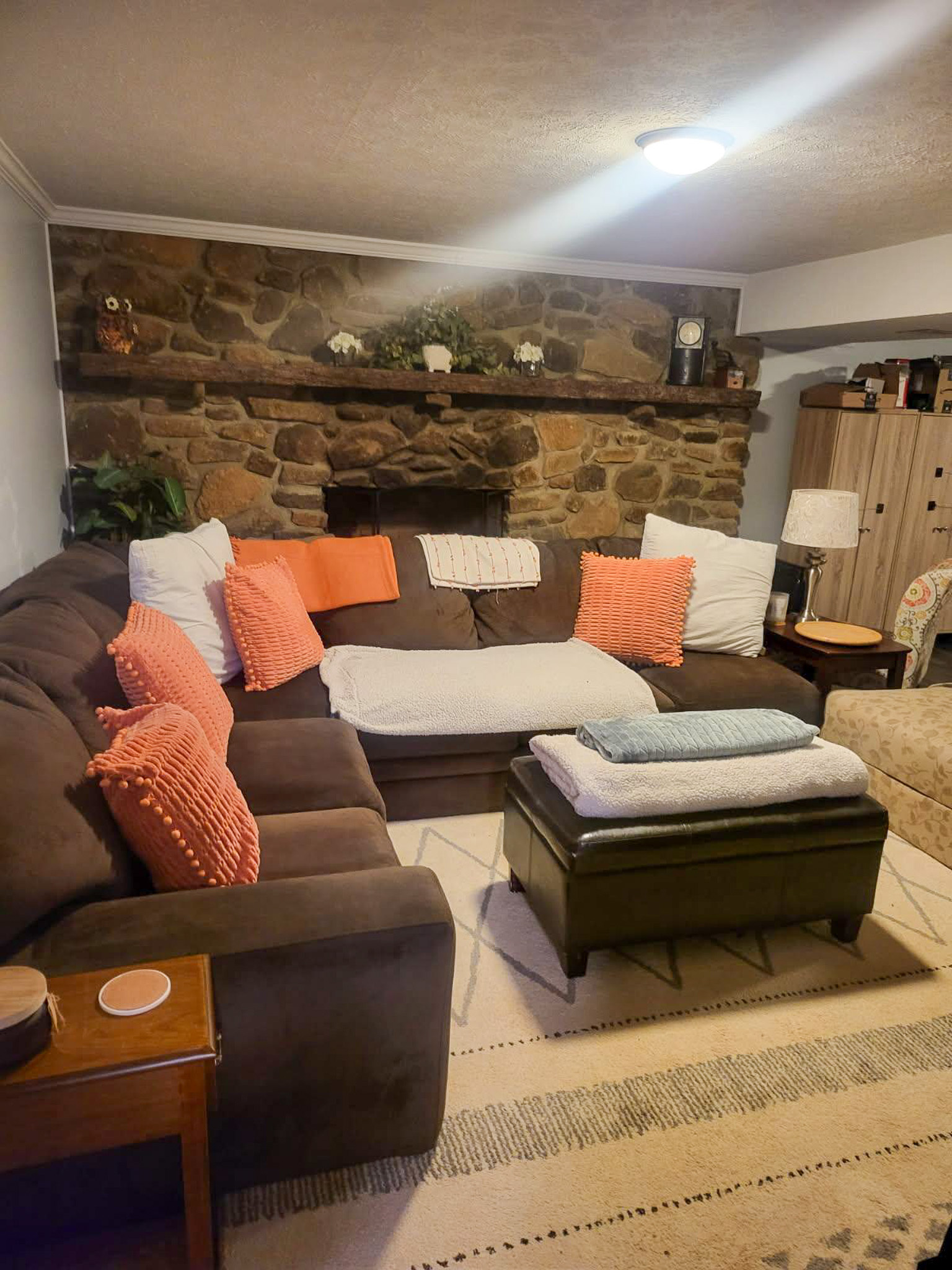 A brown sectional sofa with coral pillows sits in front of a stone fireplace wall in a softly lit living room  inside the home of Sponsored Residential Providers Scott and Tedra Flanders in Lynchburg, Virginia.
