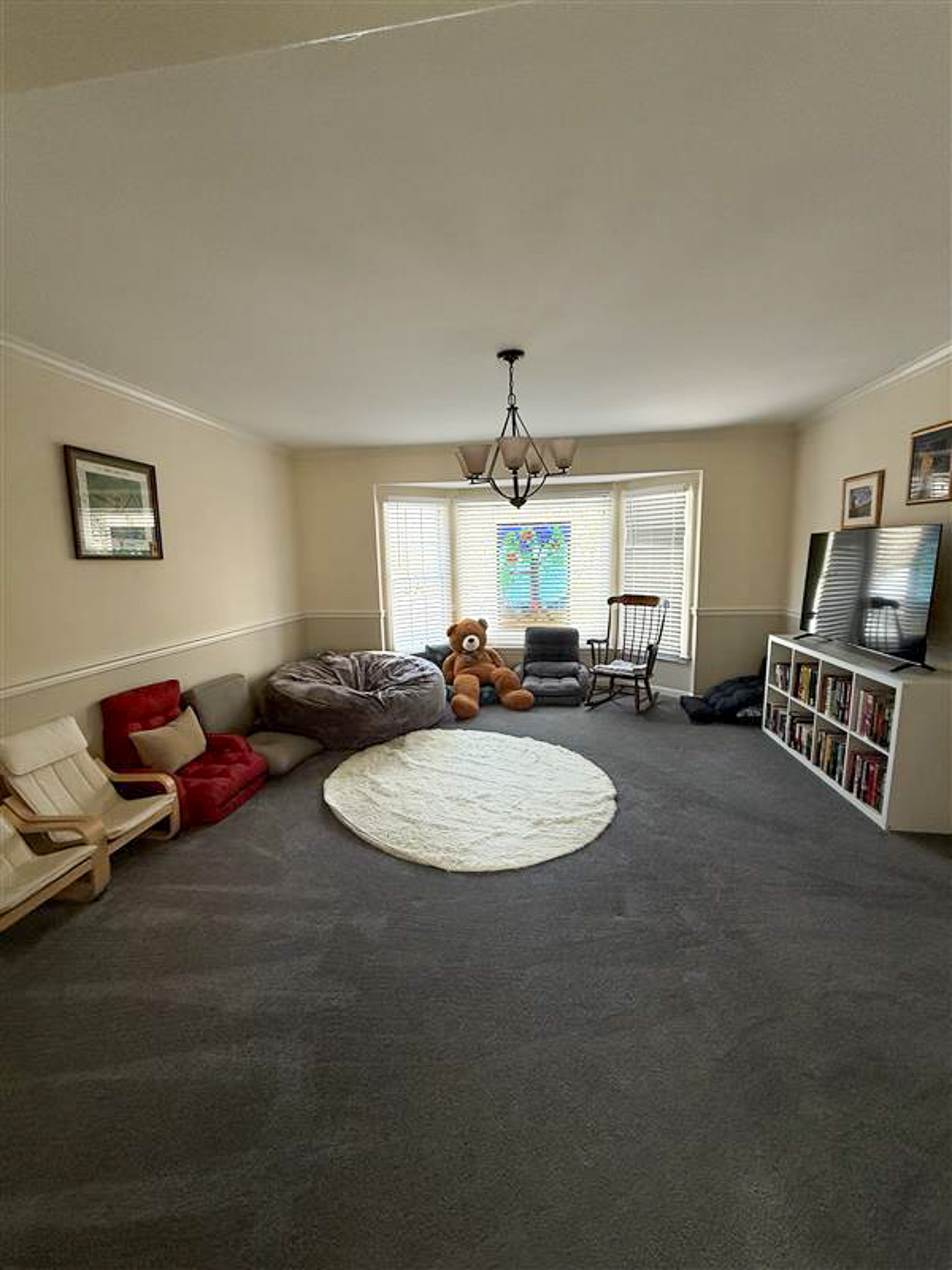 Large sitting room with carpet, floor seating, bookshelf, rocking chair, and large window inside the home of Sponsored Residential Provider Gamu Gomo in Woodbridge, Virginia.