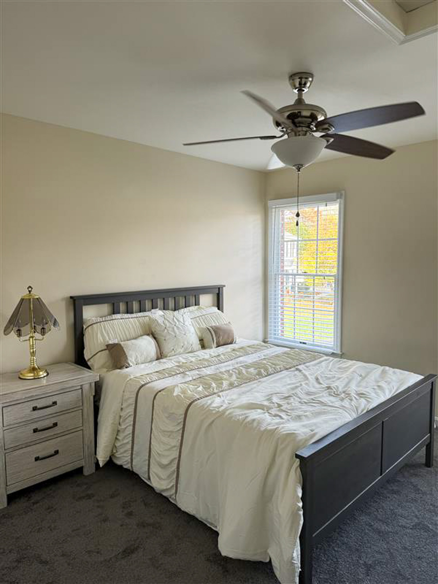 Bedroom with full-size bed, light bedding, nightstand, and ceiling fan inside the home of Sponsored Residential Provider Gamu Gomo in Woodbridge, Virginia.