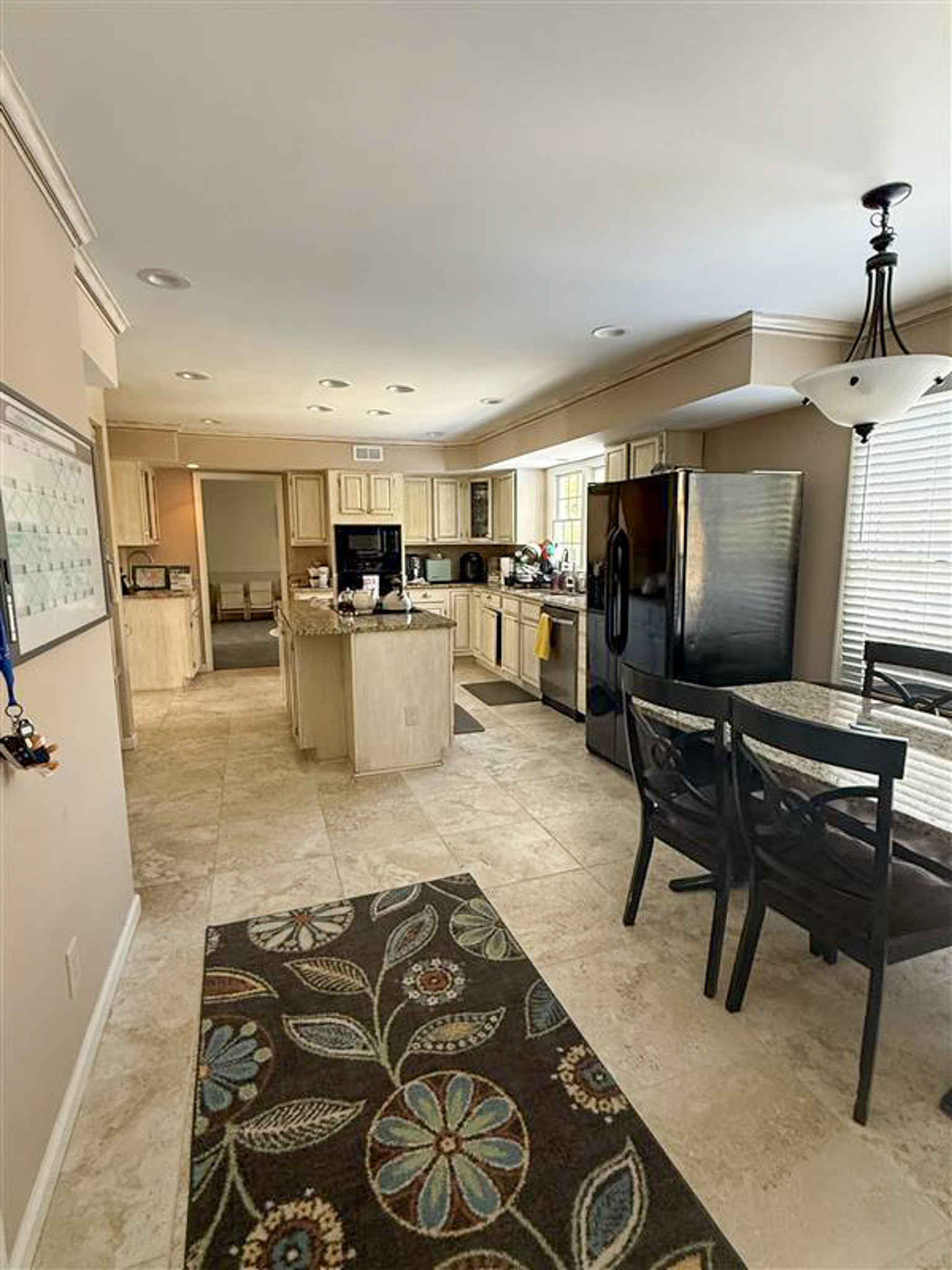 Spacious kitchen with island, light cabinetry, dining table, and stainless steel refrigerator inside the home of Sponsored Residential Provider Gamu Gomo in Woodbridge, Virginia.