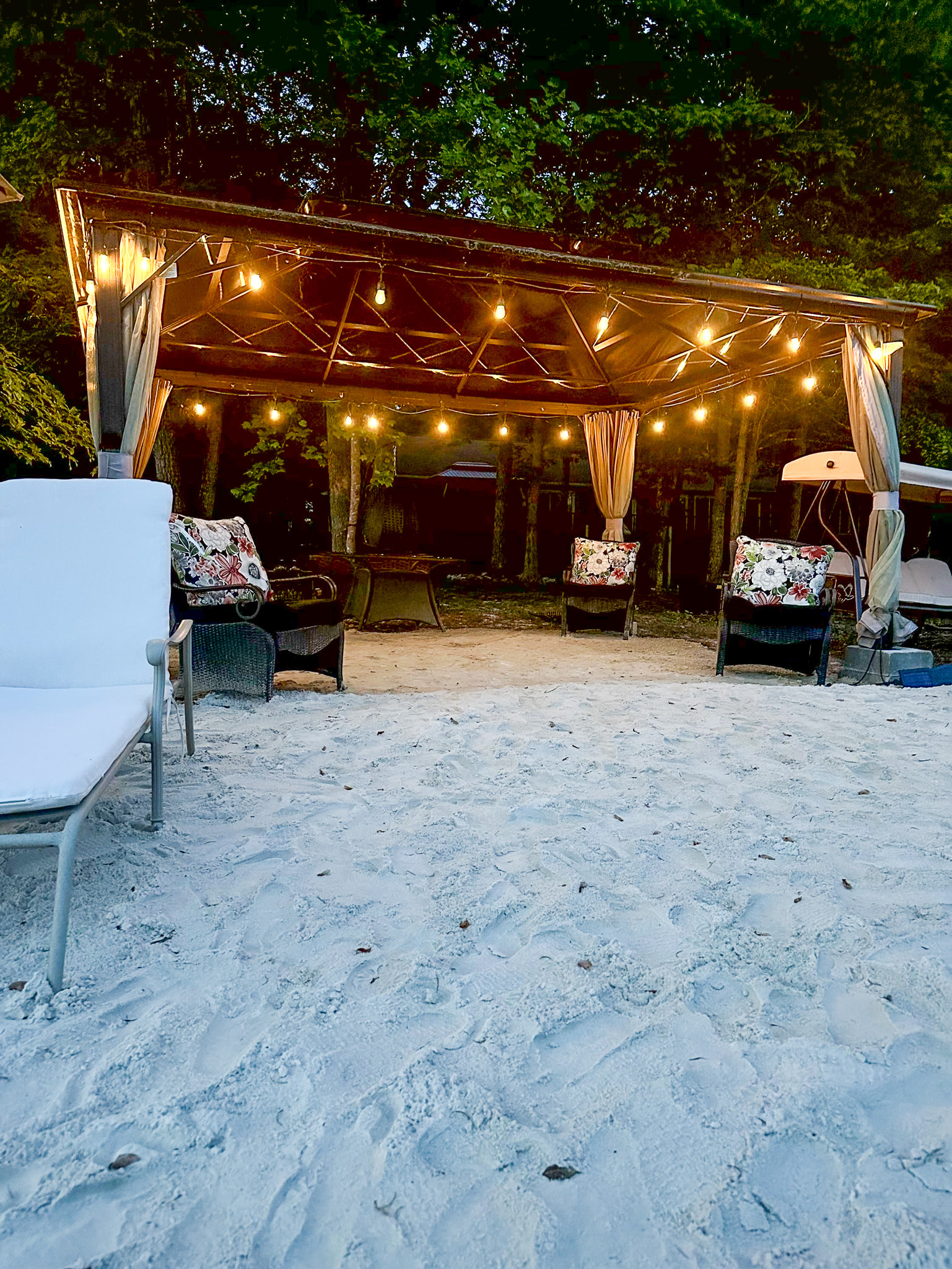 Gazebo decorated with warm string lights at dusk, viewed from a sandy beach with lounge chairs outside the home of Group Home Provider Ana Garcia in Spotsylvania, Virginia.