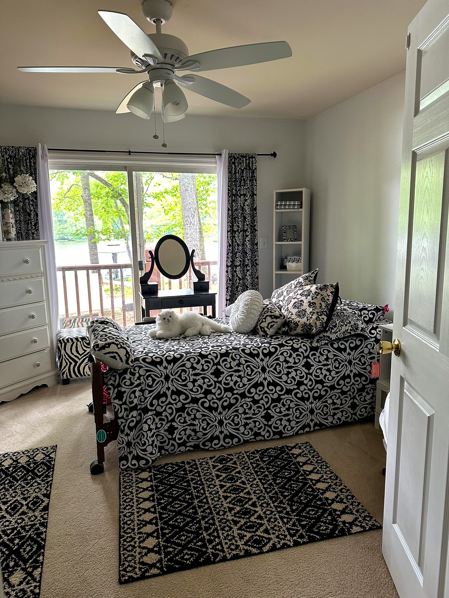 Bedroom with black‑and‑white patterned furniture and rugs, a daybed facing a window, and a ceiling fan overhead with view of lake out of sliding glass door in the home of Group Home Provider Ana Garcia in Spotsylvania, Virginia.