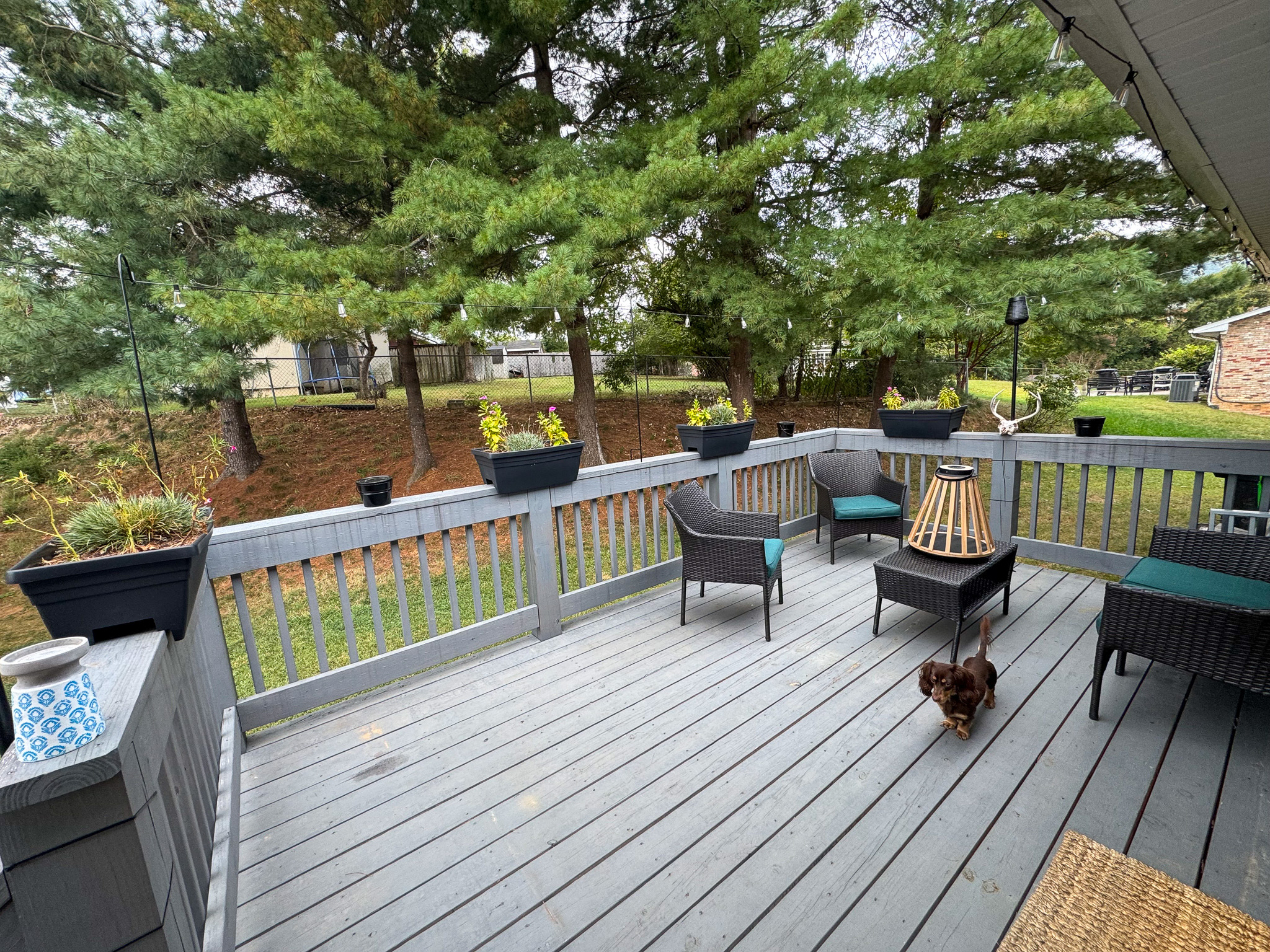 A wooden deck with outdoor seating and planters, overlooking a grassy yard bordered by tall trees at the home of Sponsored Residential Providers Hadassah Hawks and Antonio Hernandez in Salem, Virginia.