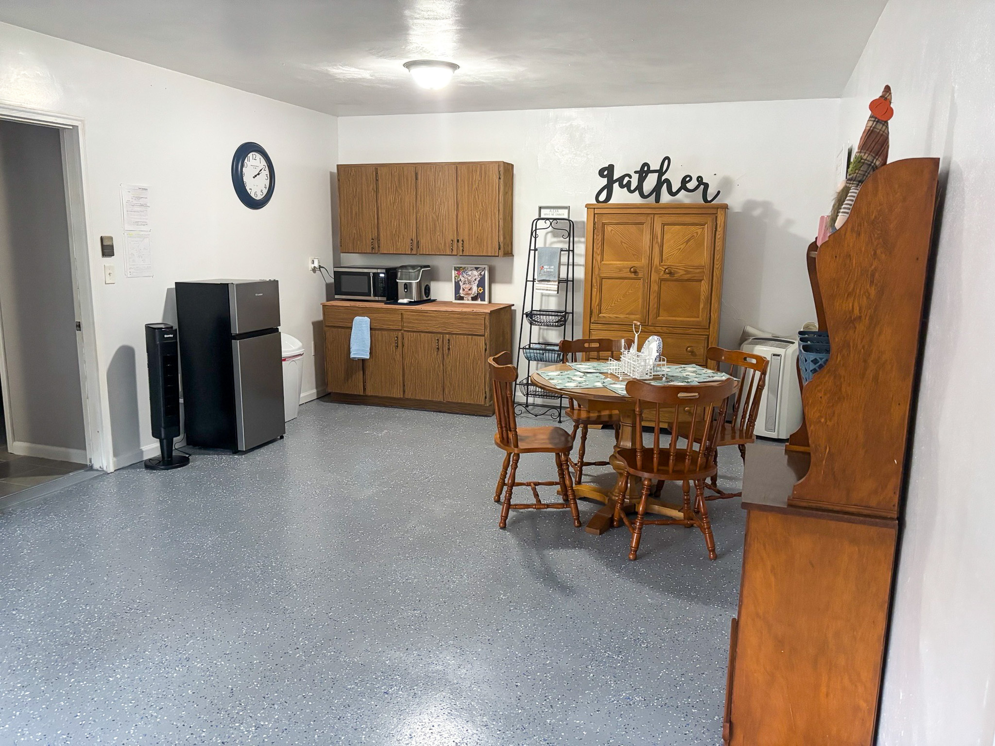 An open dining and kitchenette area with a wooden table and chairs, wooden cabinets, a small refrigerator, and shelving with kitchen items inside the home of Sponsored Residential Providers Hadassah Hawks and Antonio Hernandez in Salem, Virginia.