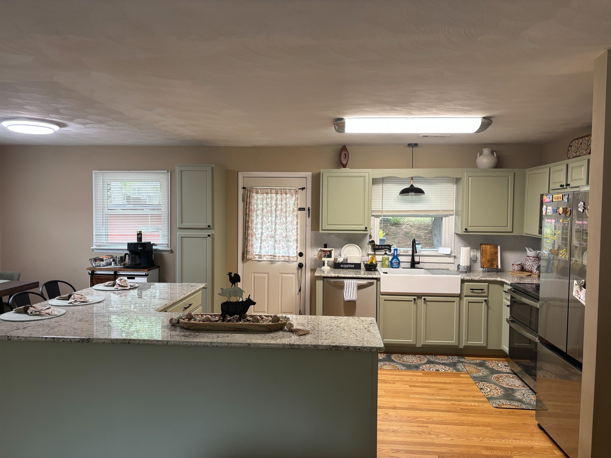 A kitchen with light green cabinets, a granite peninsula, a farmhouse sink, and a dining area visible to the left inside the home of Sponsored Residential Providers Hadassah Hawks and Antonio Hernandez in Salem, Virginia.
