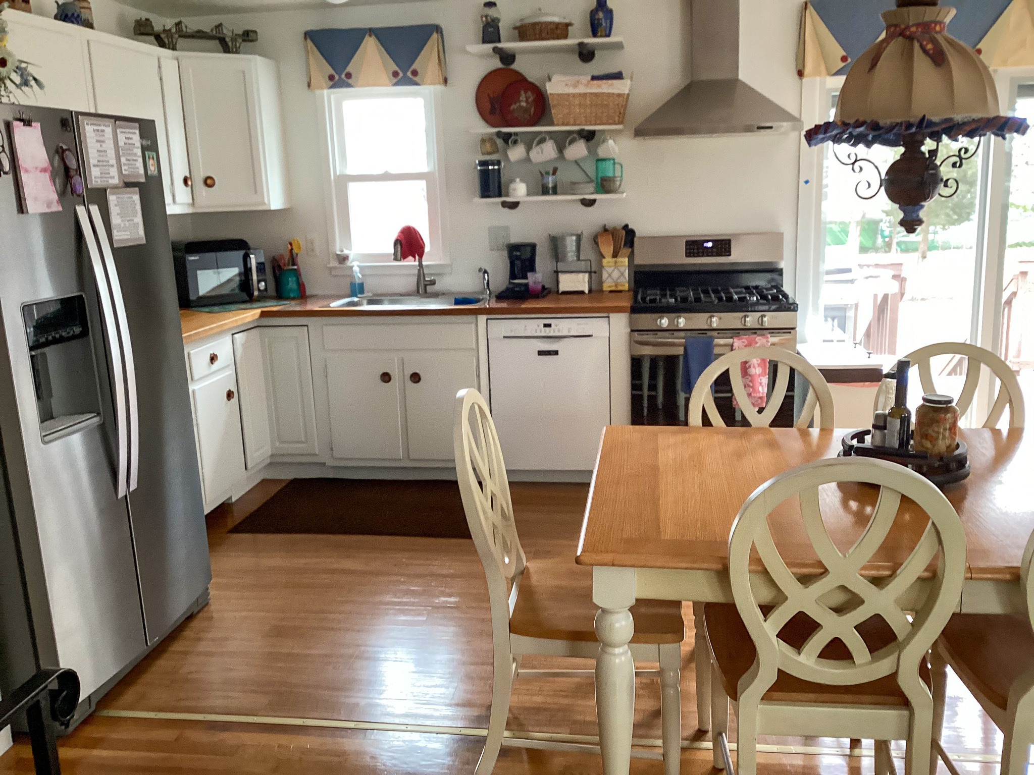 A bright kitchen with white cabinets, stainless steel appliances, open shelves, and a wooden dining table with four chairs, inside the home of Sponsored Residential Providers Teresa and Billy Herran in Woodbridge, Virginia.