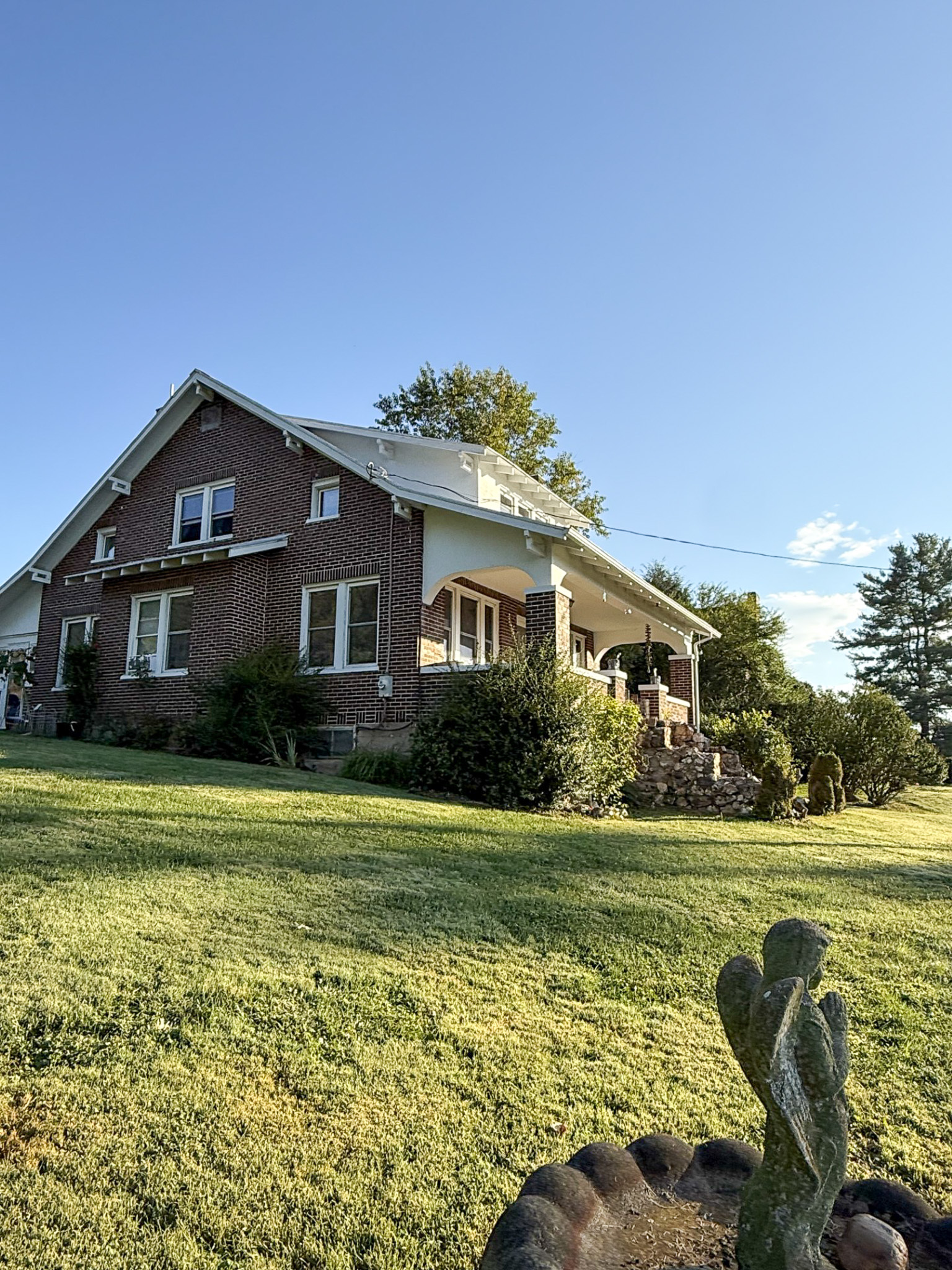 Brick house with a large sloped lawn in bright sunlight, viewed from a low angle with a small cactus in the foreground belonging to Sponsored Residential Provider Tammy Hunt in Floyd, Virginia.
